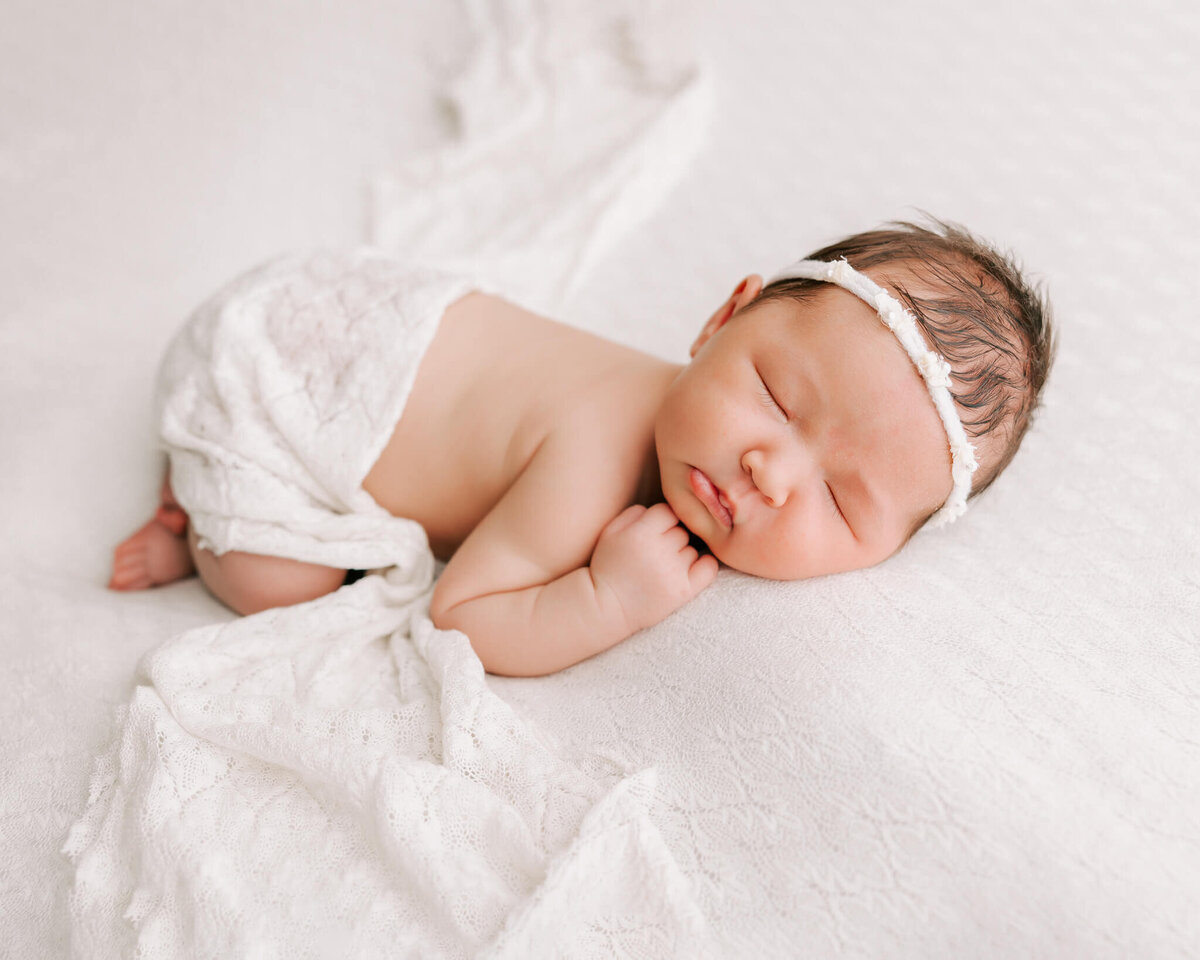 one week old girl sleeping on her stomach with her body draped in white lacy fabric