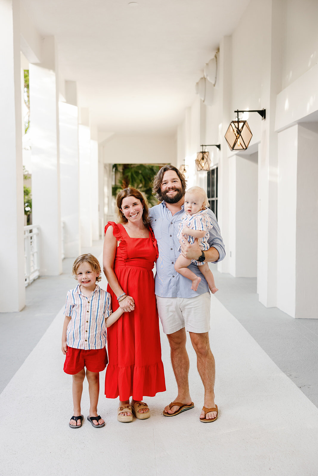 A stylish family poses in coordinated red, white, and blue outfits in a beautiful white hallway during a Florida Keys family session.
