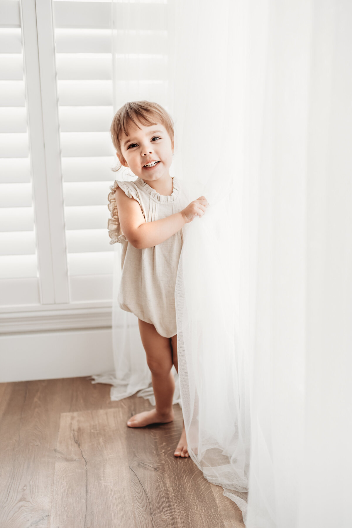 toddler girl playing in the curtains