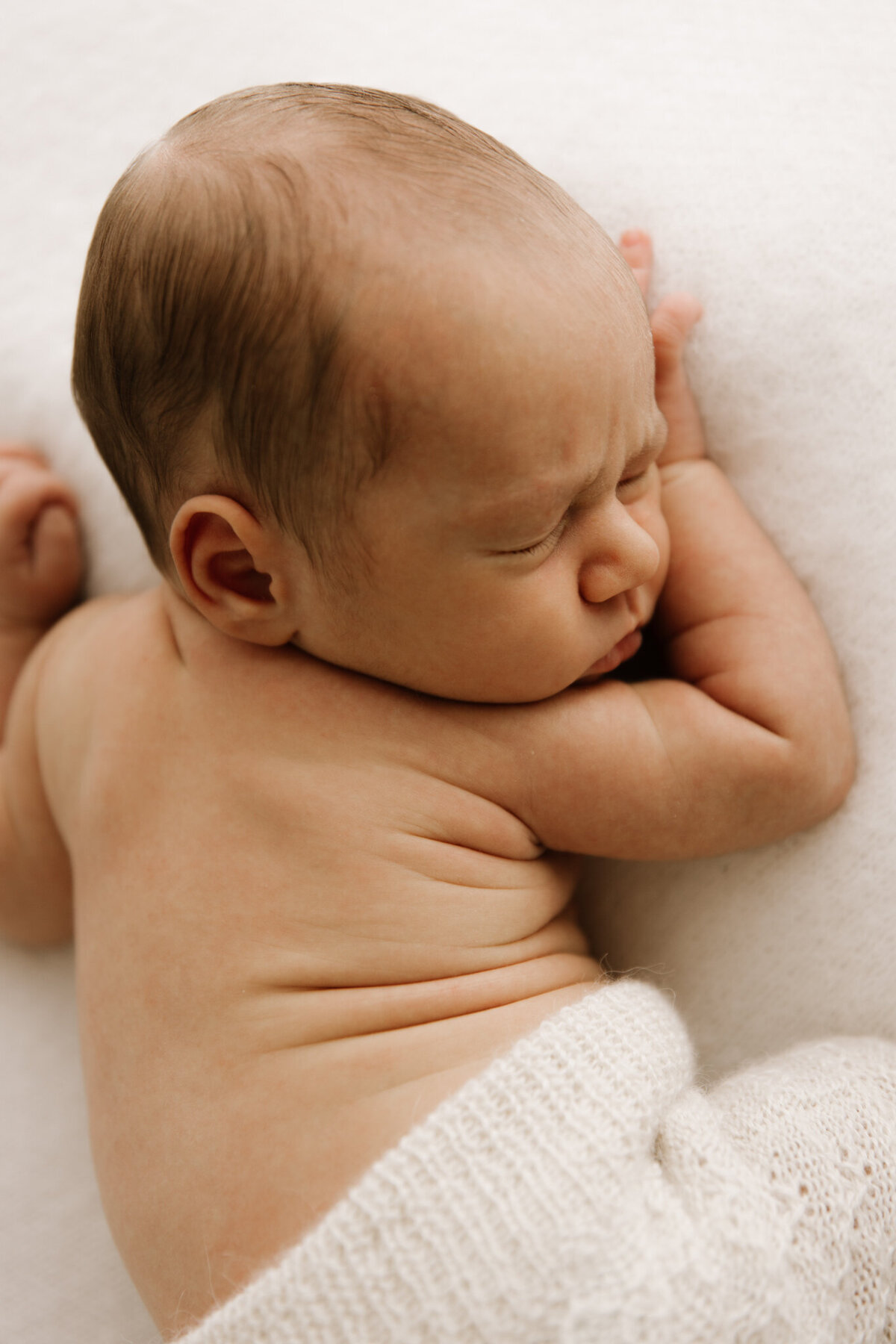 Close-up of a newborn baby peacefully sleeping on a soft white blanket, showing delicate skin folds and gentle textures in a softly lit Southwest Sydney studio.