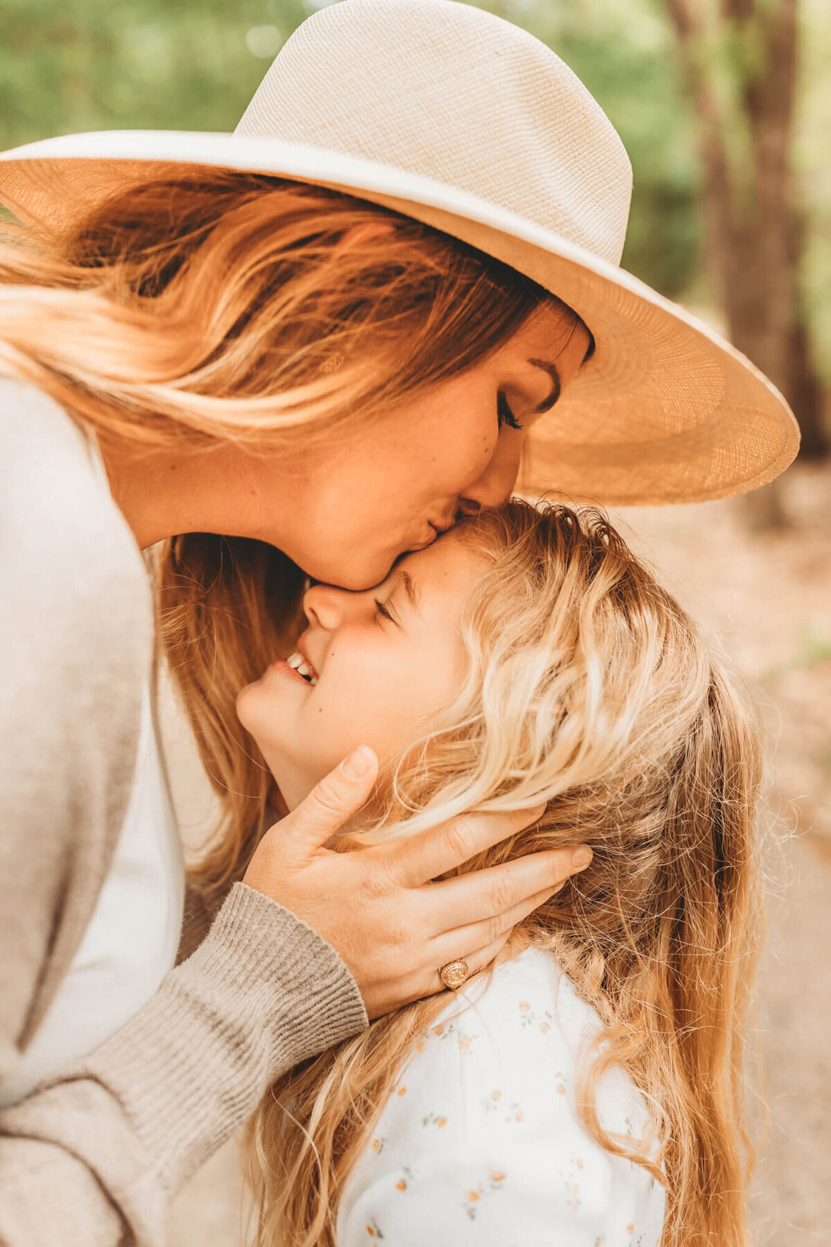 mother kisses daughter on the forehead while wearing a neutral sweater and taupe hat.