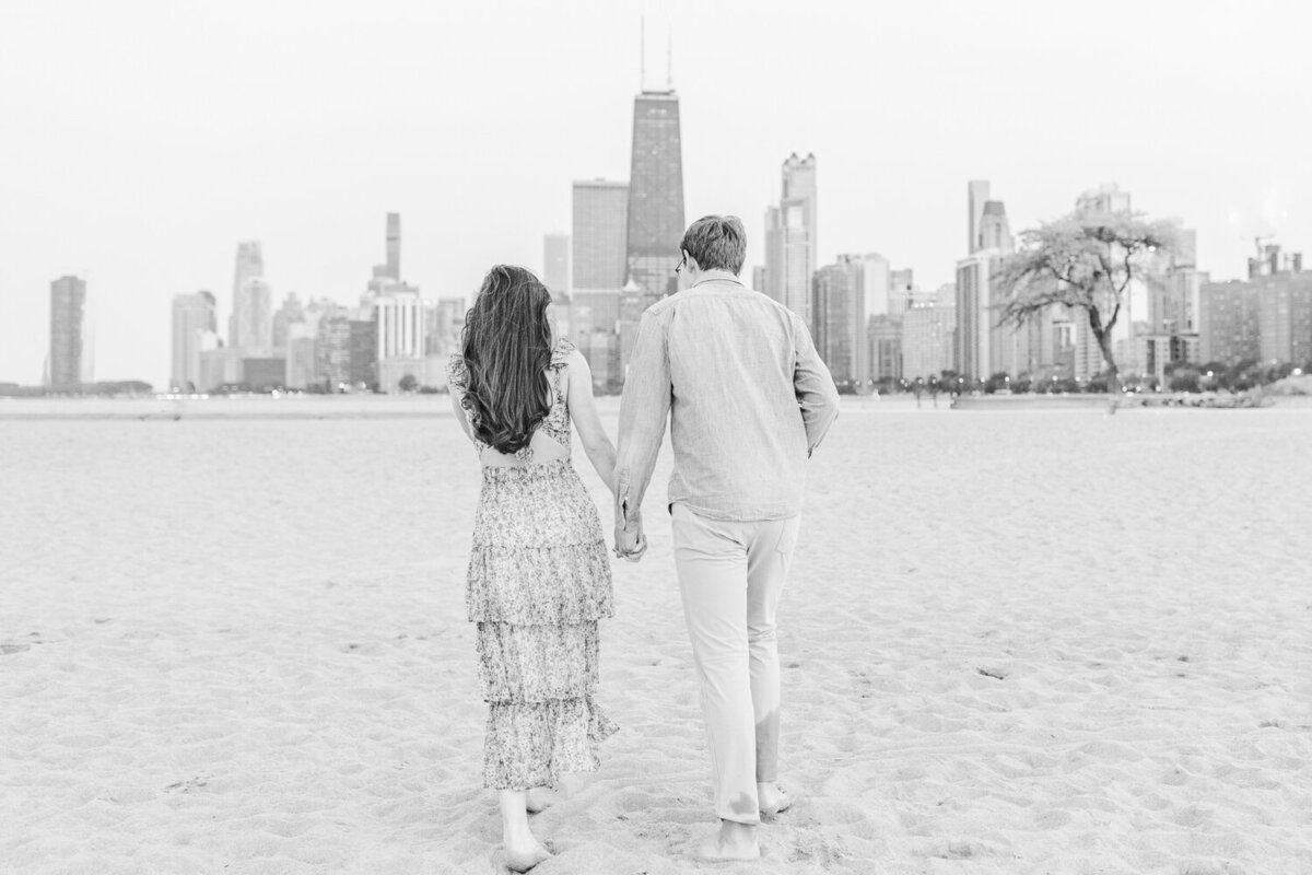 a couple holding hands while walking on the beach with the city in the background