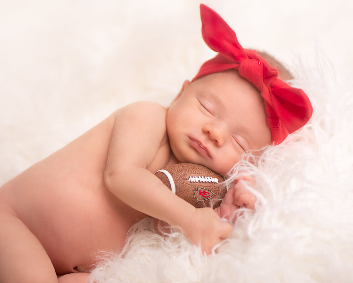 Football Chiefs newborn portrait with a  tiny football, captured in Overland Park, Kansas. Ideal for families seeking holiday-themed newborn photography in the Kansas City metro area.