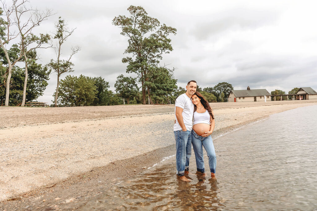 Connecticut maternity photographer captures couple standing in shallow water wearing denim