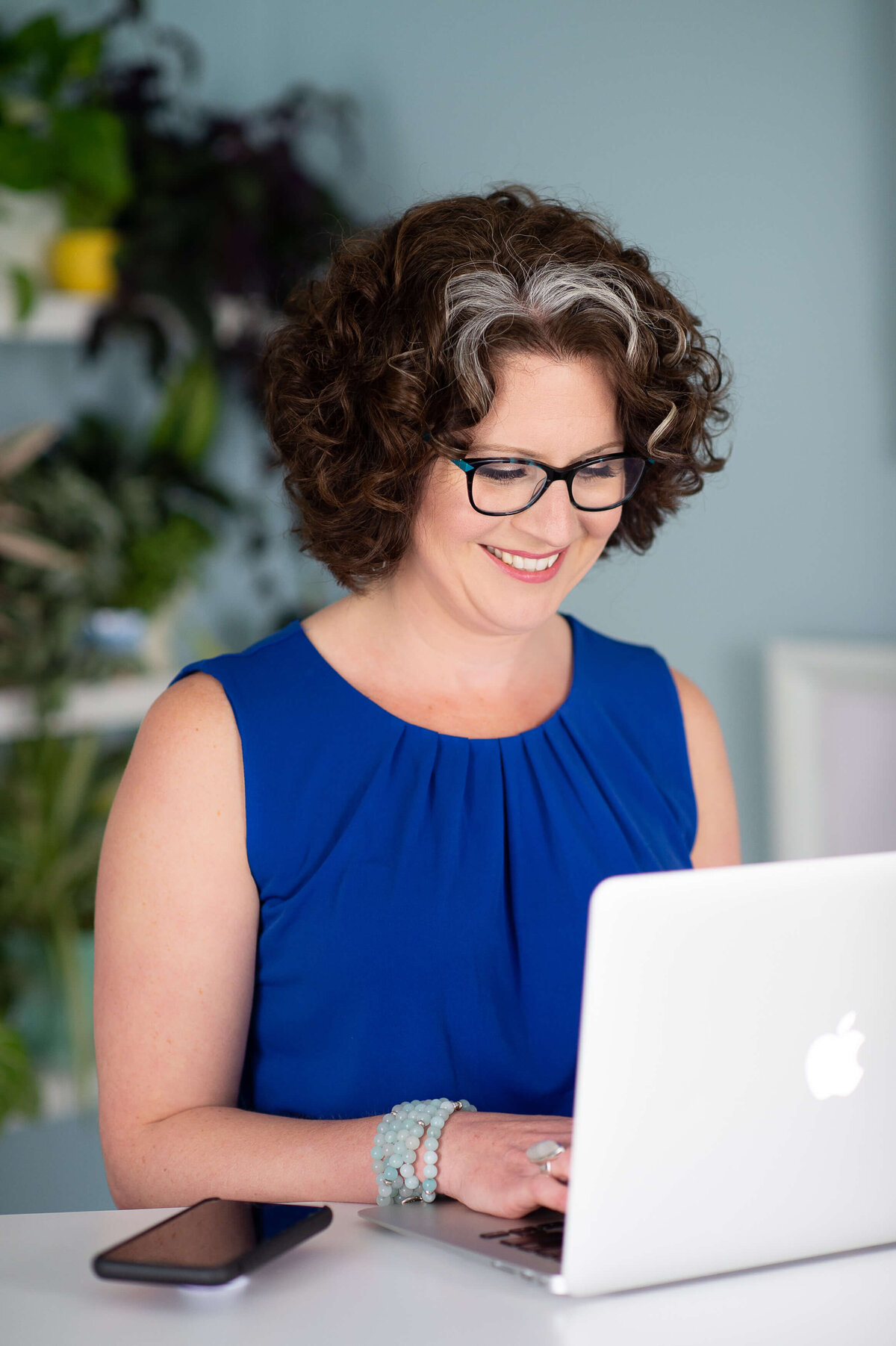 Ottawa Branding Photographer of a woman in a blue blouse and black glasses typing on her laptop in her home office.  Captured by JEMMAN Photography COMMERCIAL