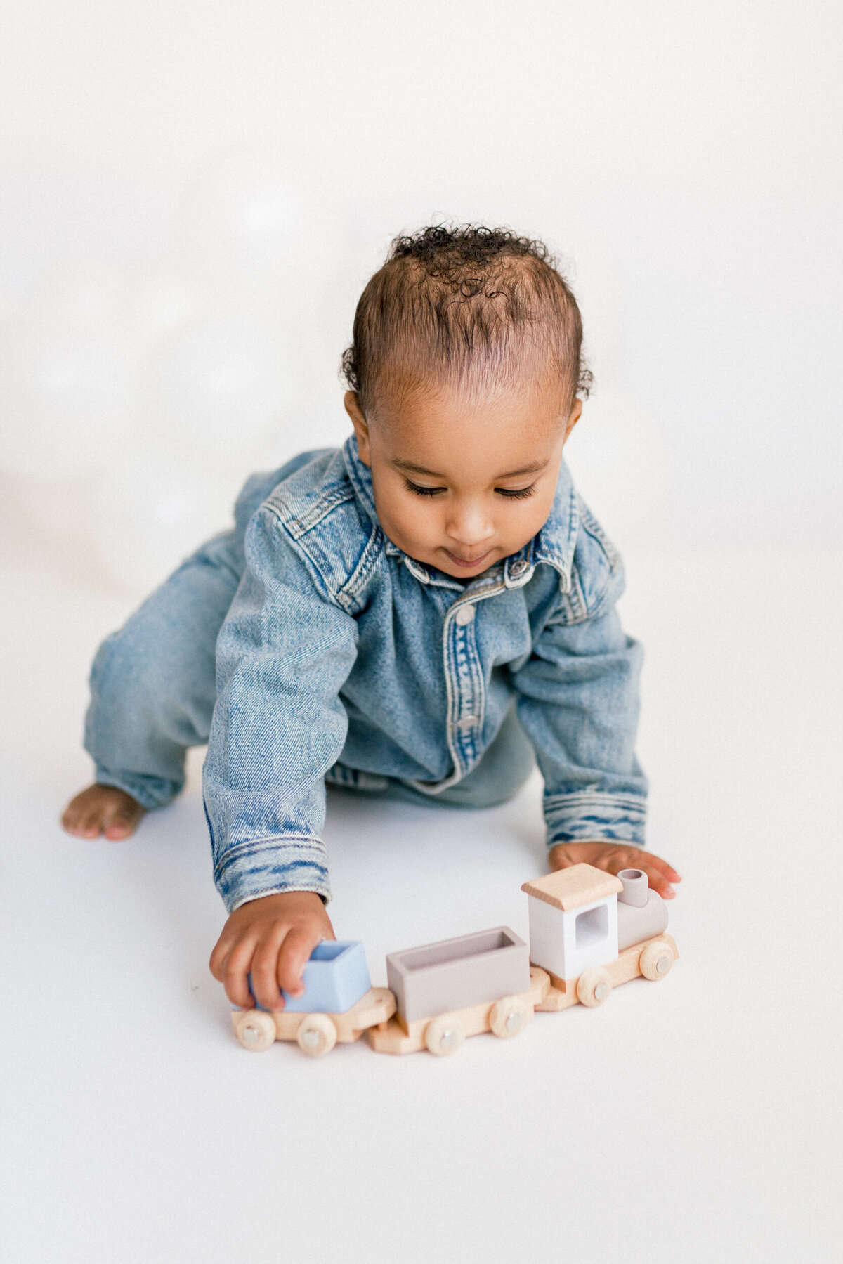littl eboy in blue denim outfit playing with a toy wooden train during his first birthday photo session with renee ash photography  newton nj 