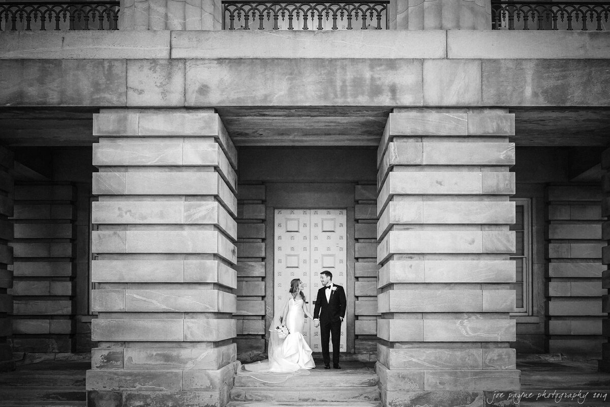 A wedding couple holding hands and standing outside a large building.