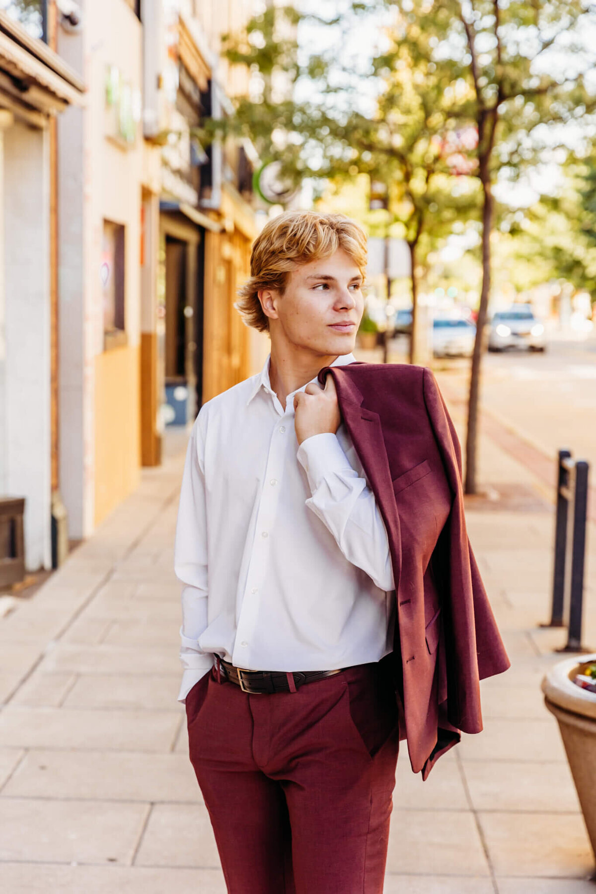 young man looking over his shoulder as he holds his suit jacket on shoulder downtown Neenah.