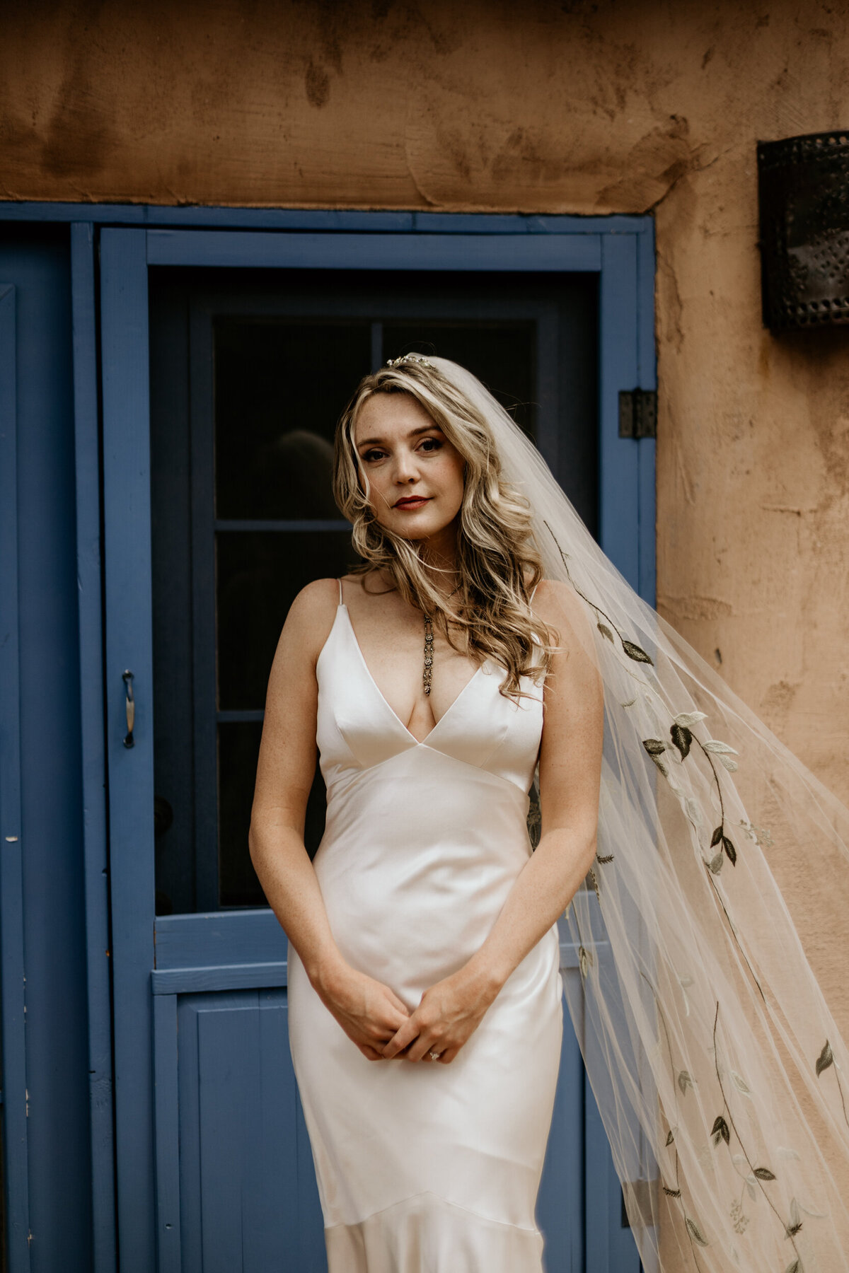 bride stanging in front of a turquoise door with a long embroidered veil