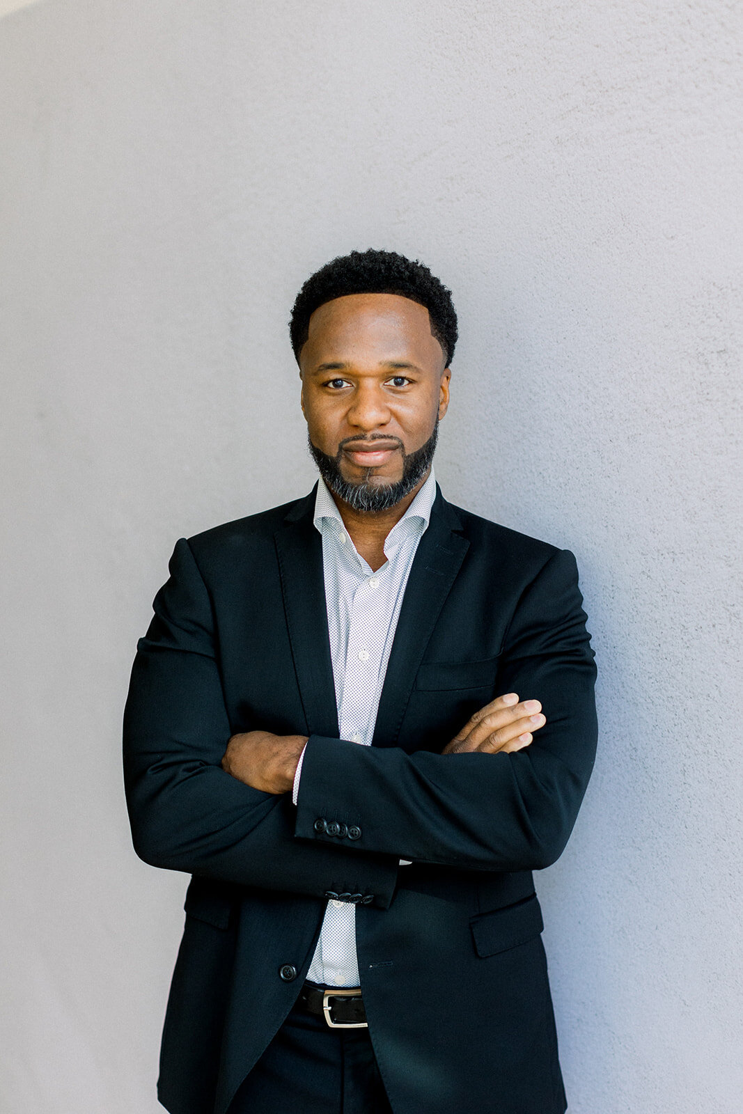 Brand headshot of a man in a navy blue suit with his arms cossed