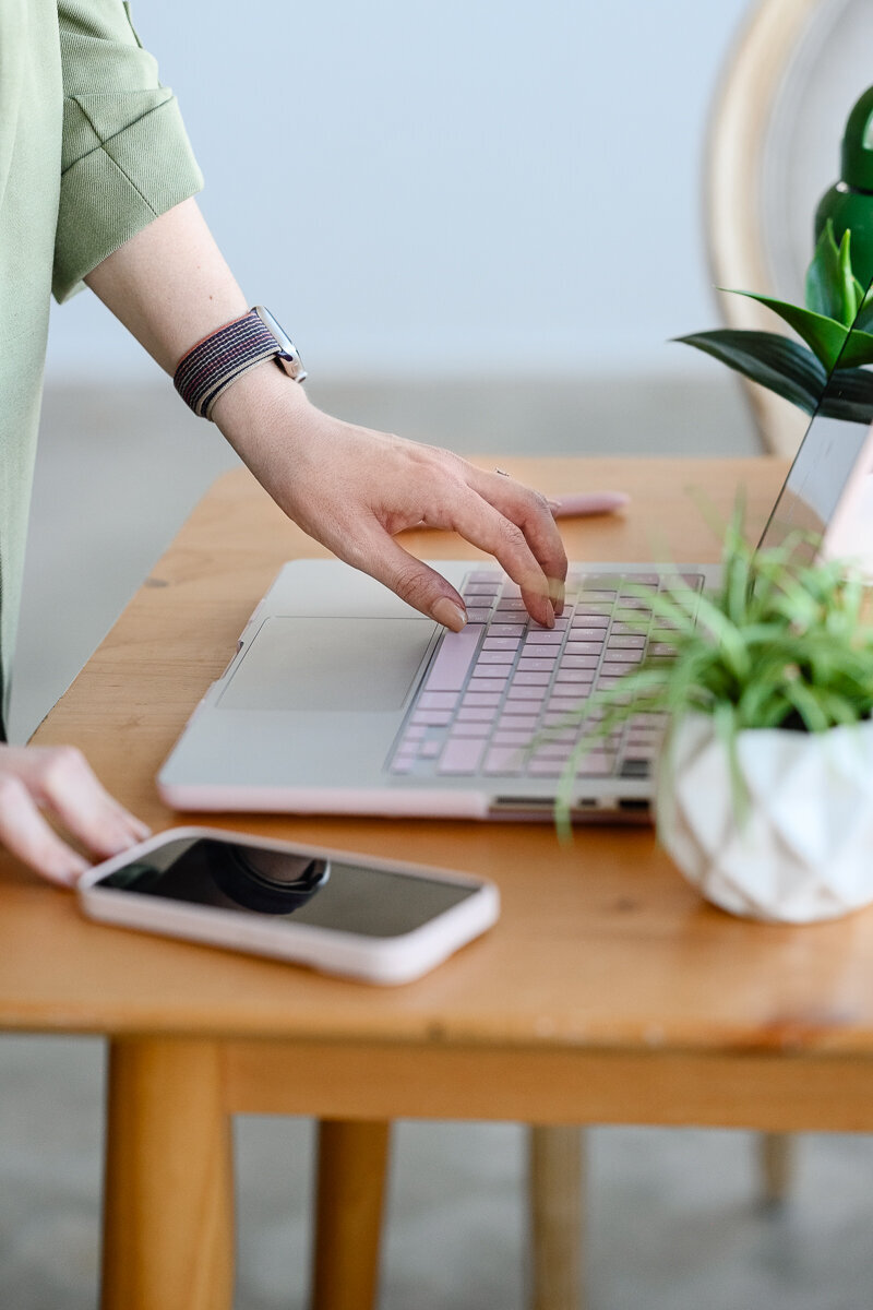 A personal branding photographer takes a photo of a woman's hand working on a computer and her phone on the desk during her branding pictures and denver branding photography session.