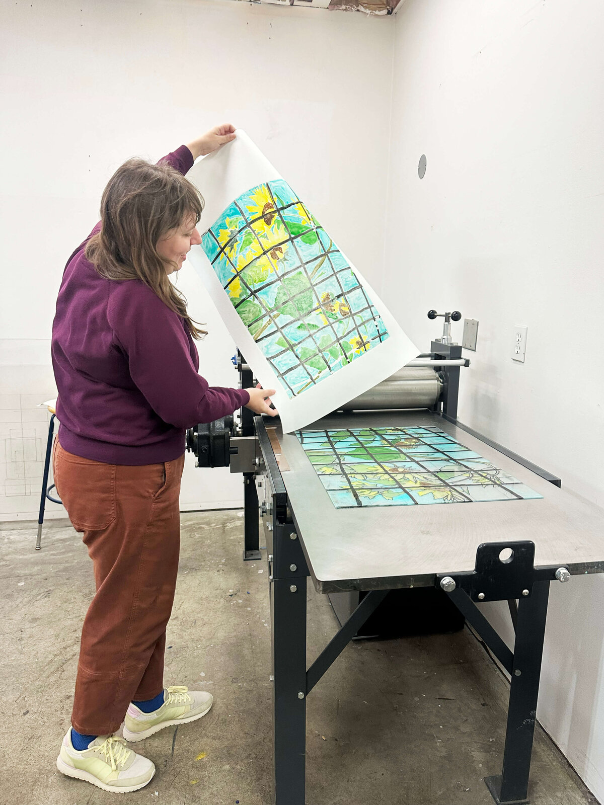 An artist pulls a large sunflower grid monoprint from the press.