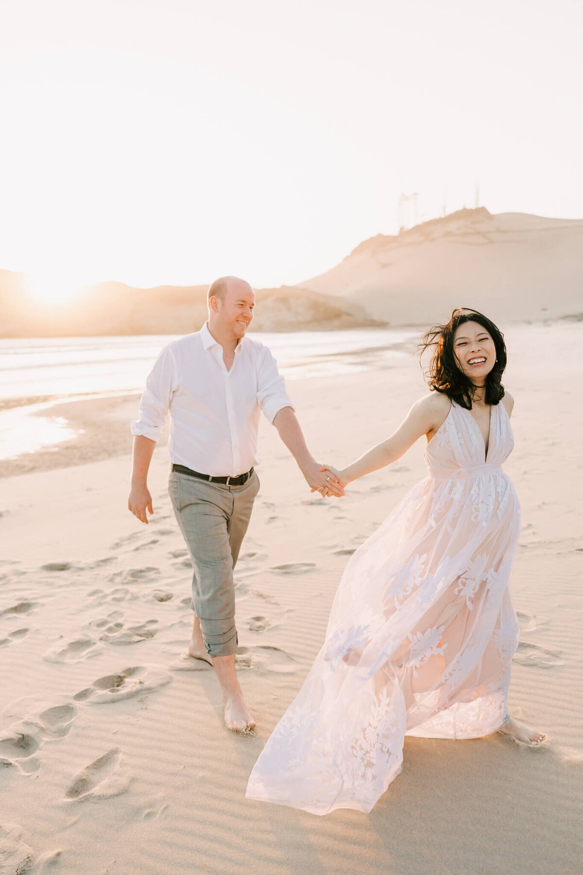 portrait fo a woman walking in front of husband. She is pregnant and smiling at the oregon coast.
