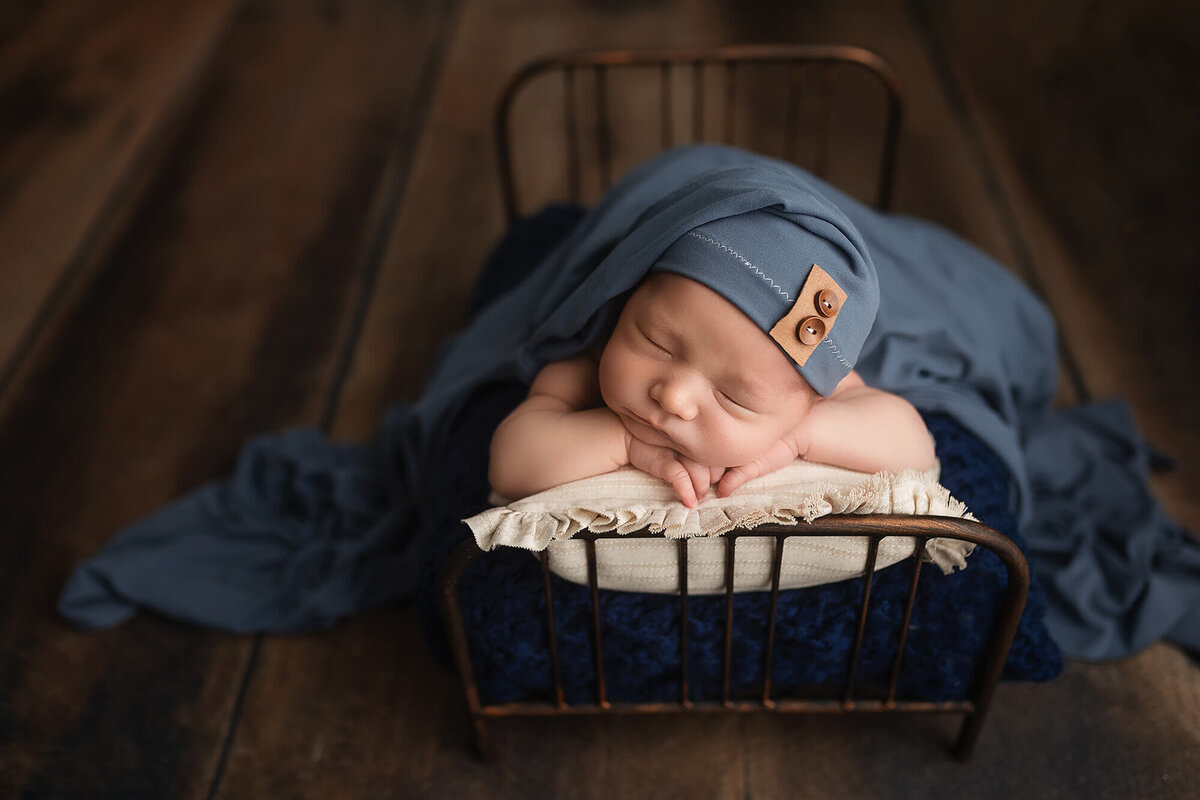Baby boy sleeping on a bed wearing a blue sleepy cap.