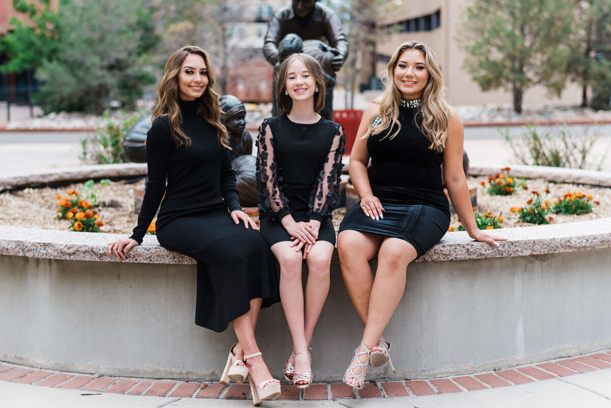Stylish sisters all sit together against a fountain during their photo session