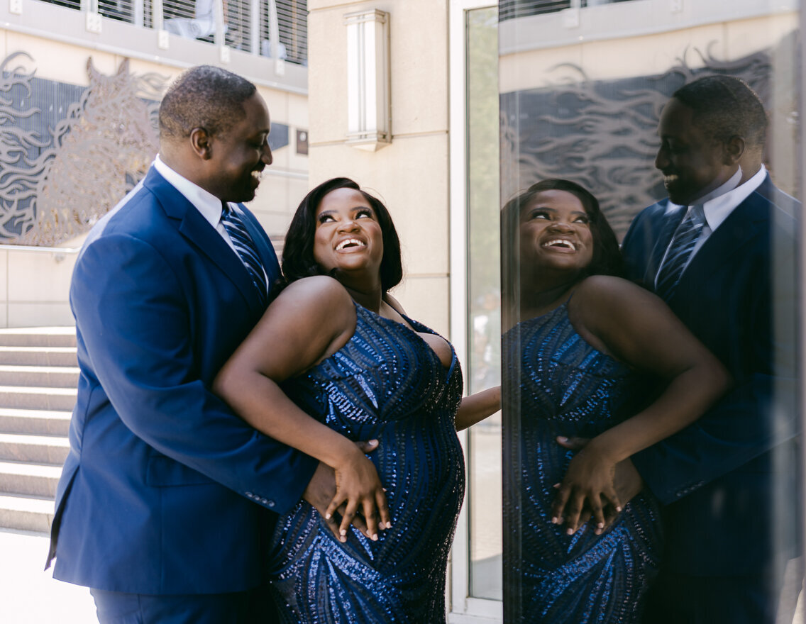 An African American couple dressed in  blue attire stare at each other and their reflection is in a window by them.