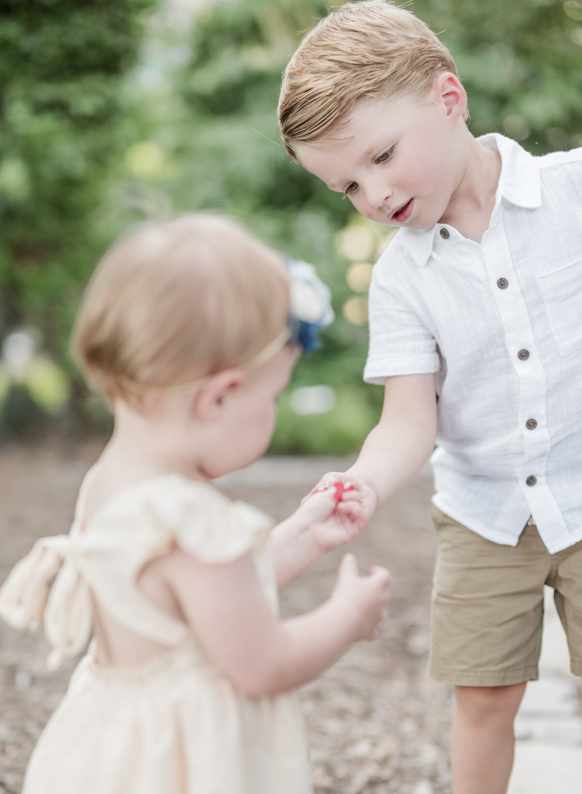 Toddler boy gently holding his little sister’s hand while standing outdoors on a garden path.