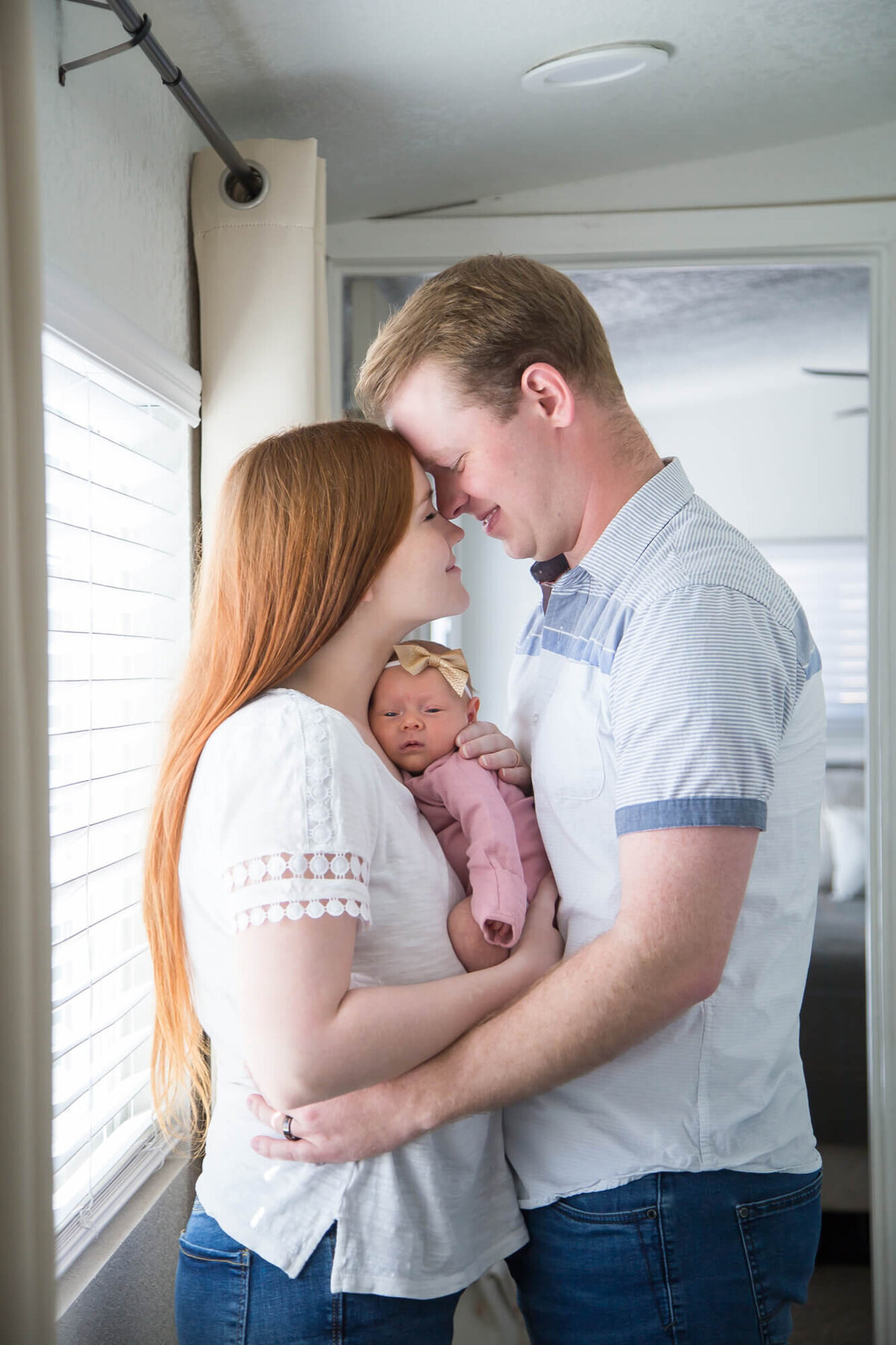 Redheaded woman and man in blue shirt holding newborn baby girl and intimately looking at each other