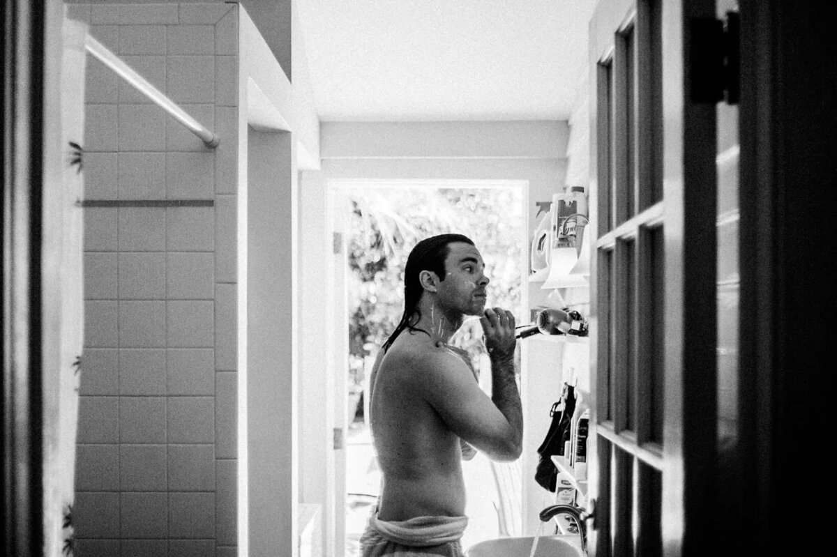 A man in a towel shaving in front of a bathroom mirror