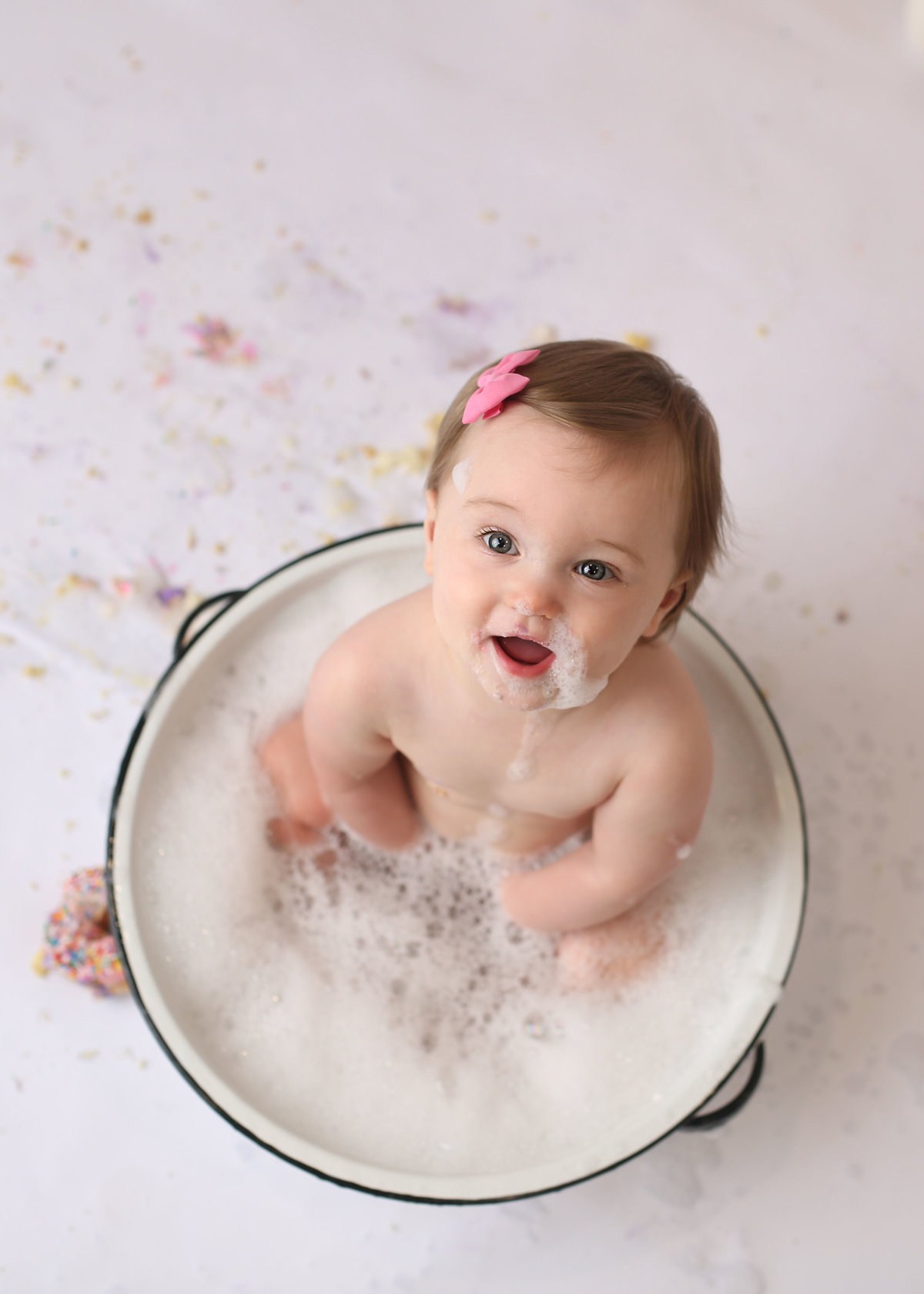 baby girl sitting in soapy water farmhouse metal tub with bubbles on face