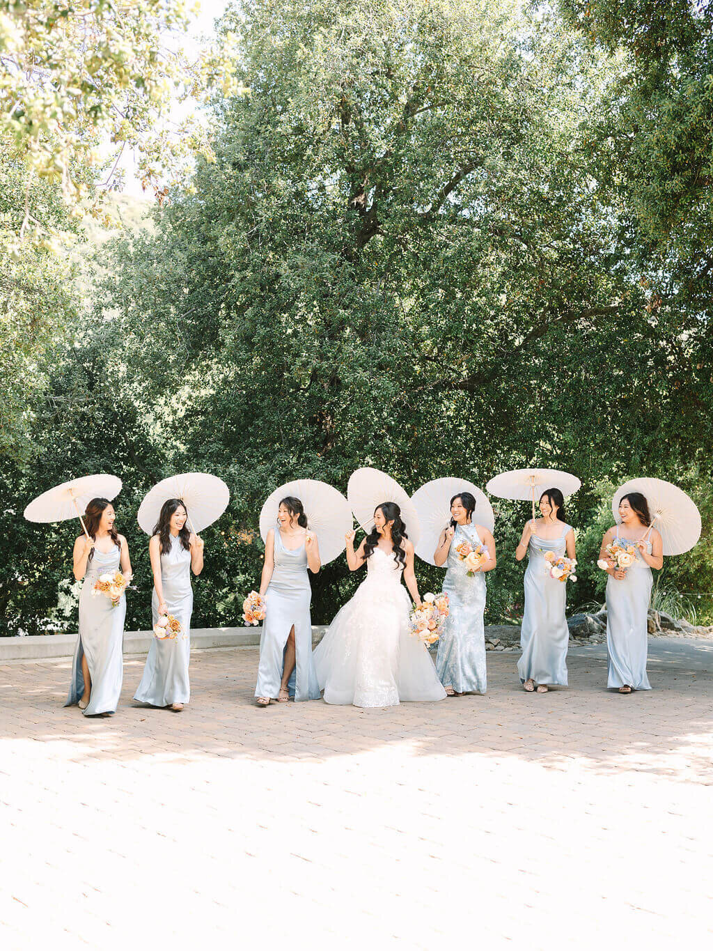wedding photography of bridesmaids wearing powder blue dresses laughing and walking with bride carrying bouquets and umbrella