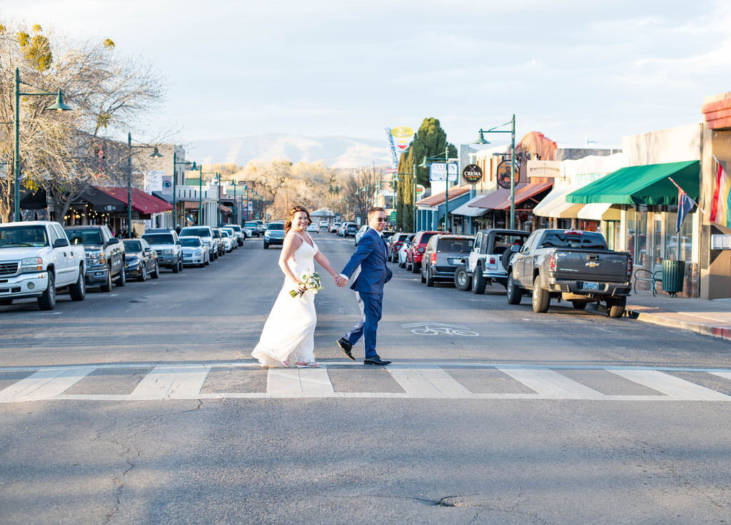 A newlywed couple holding hands and walking along a crosswalk.
