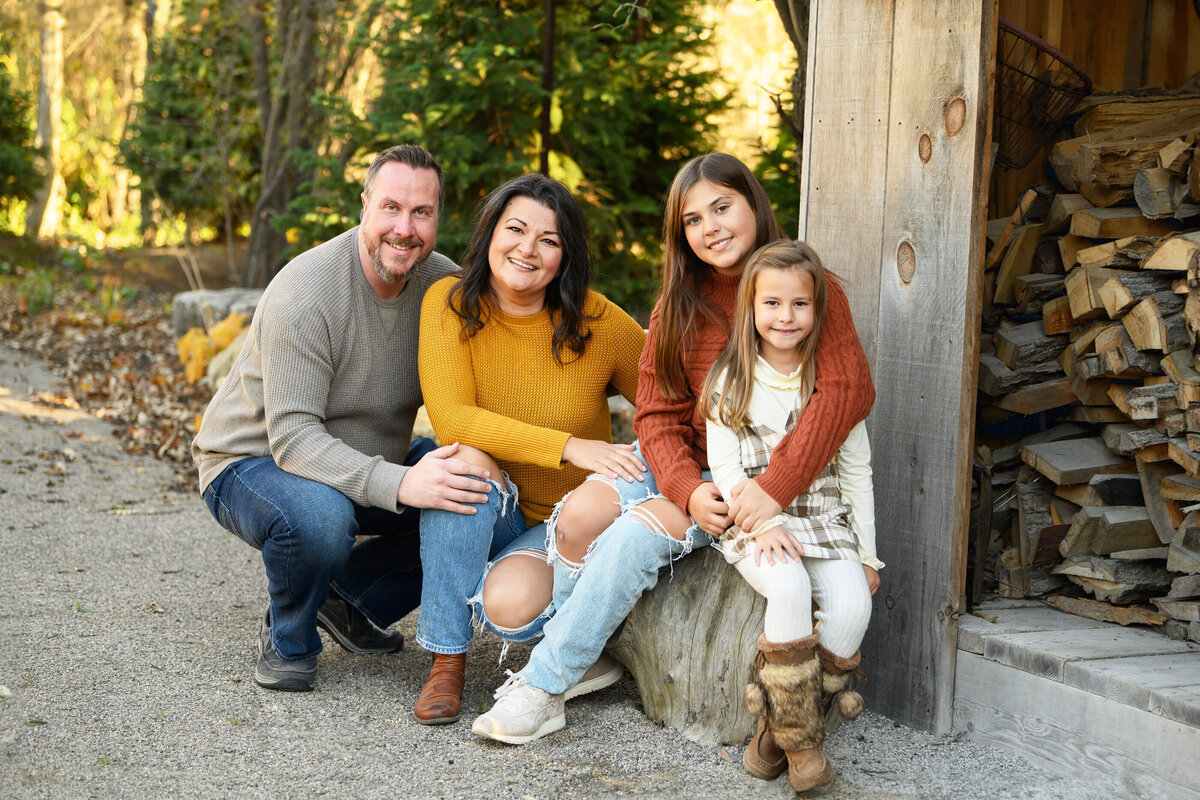 Mom and dad with their two daughters sitting near a wood shed for their fall family photography session in Burlington, On