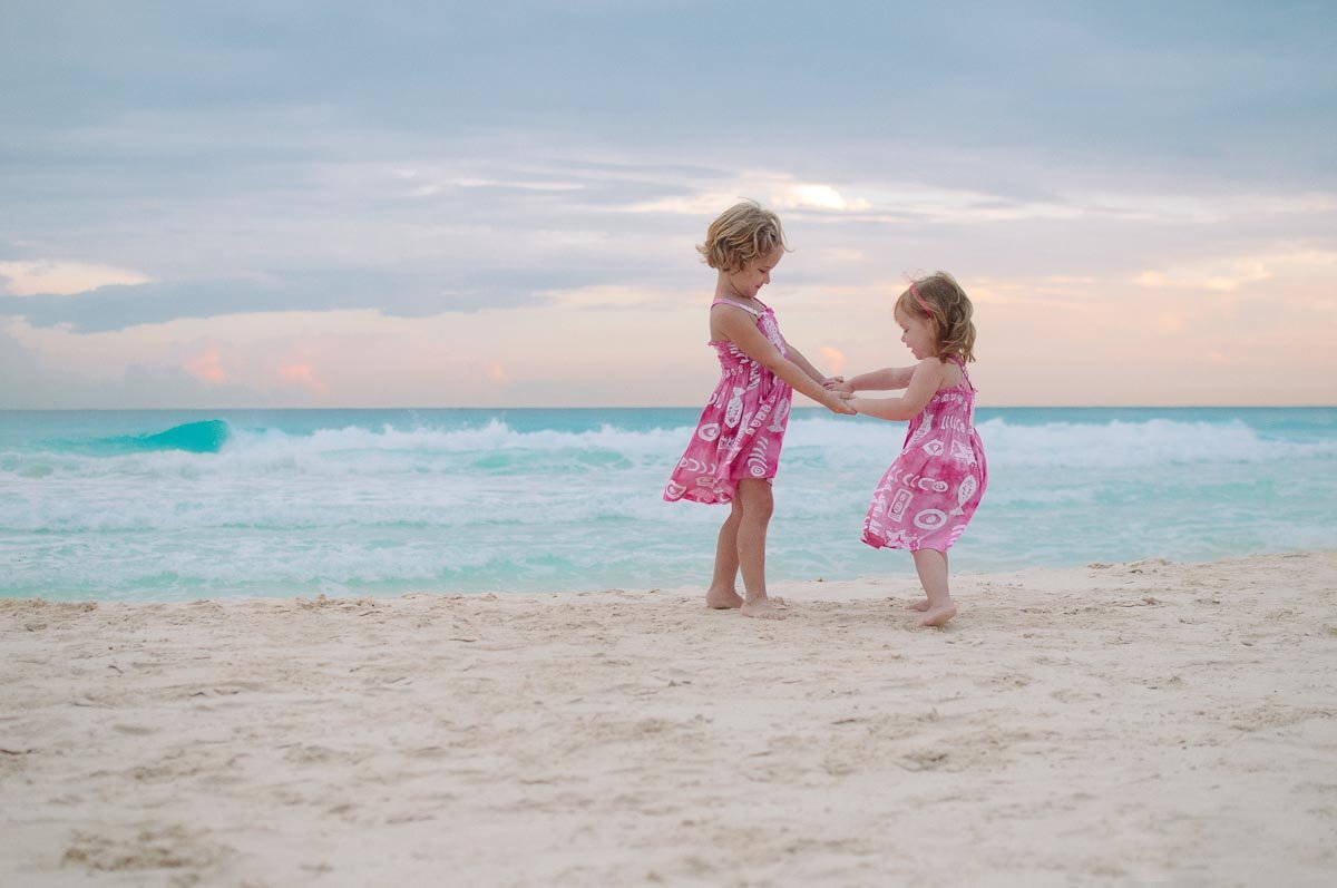young sisters in pink dressed playing on beach
