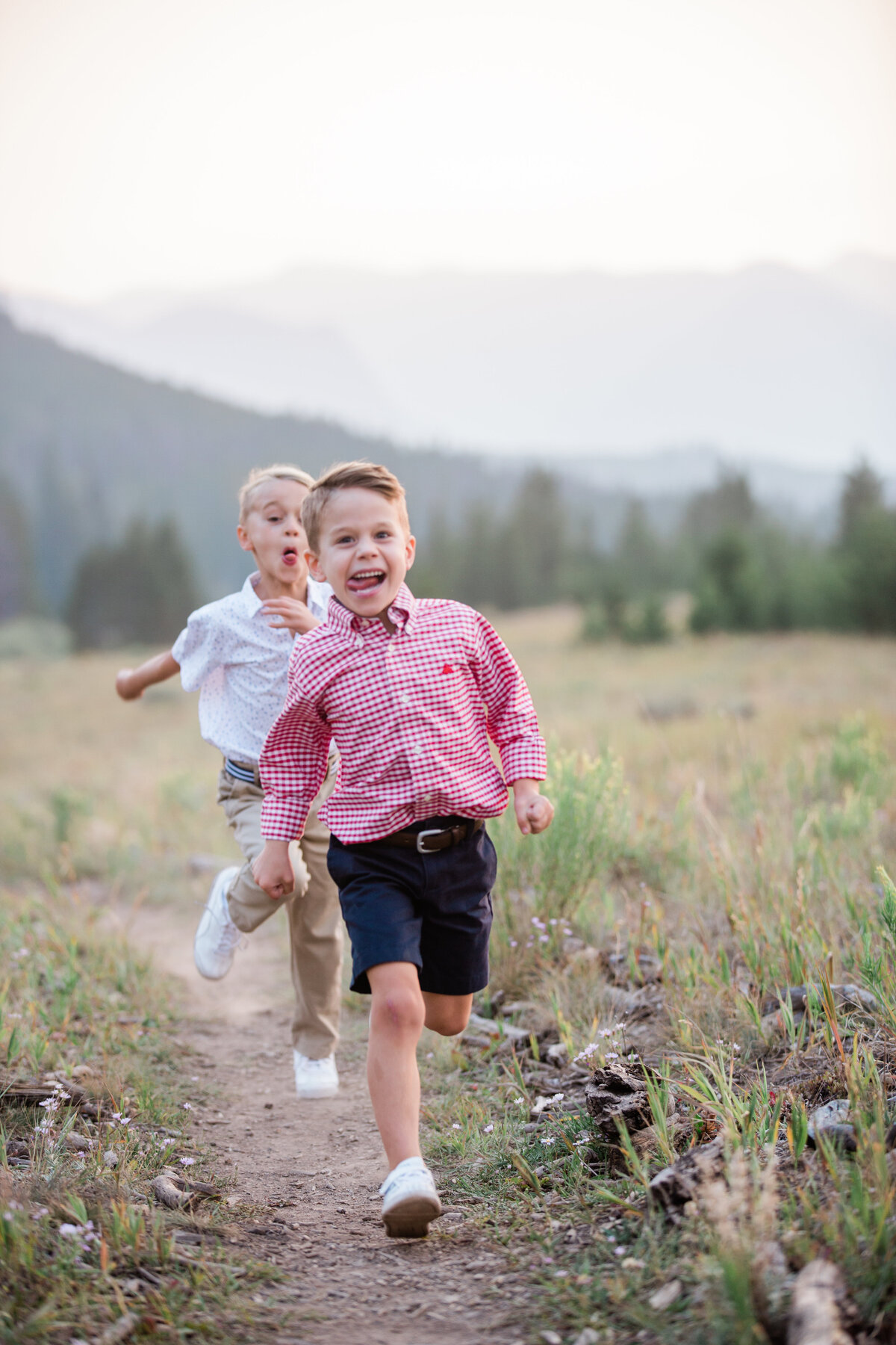Two young boys race playfully through a field with mountains in the distance