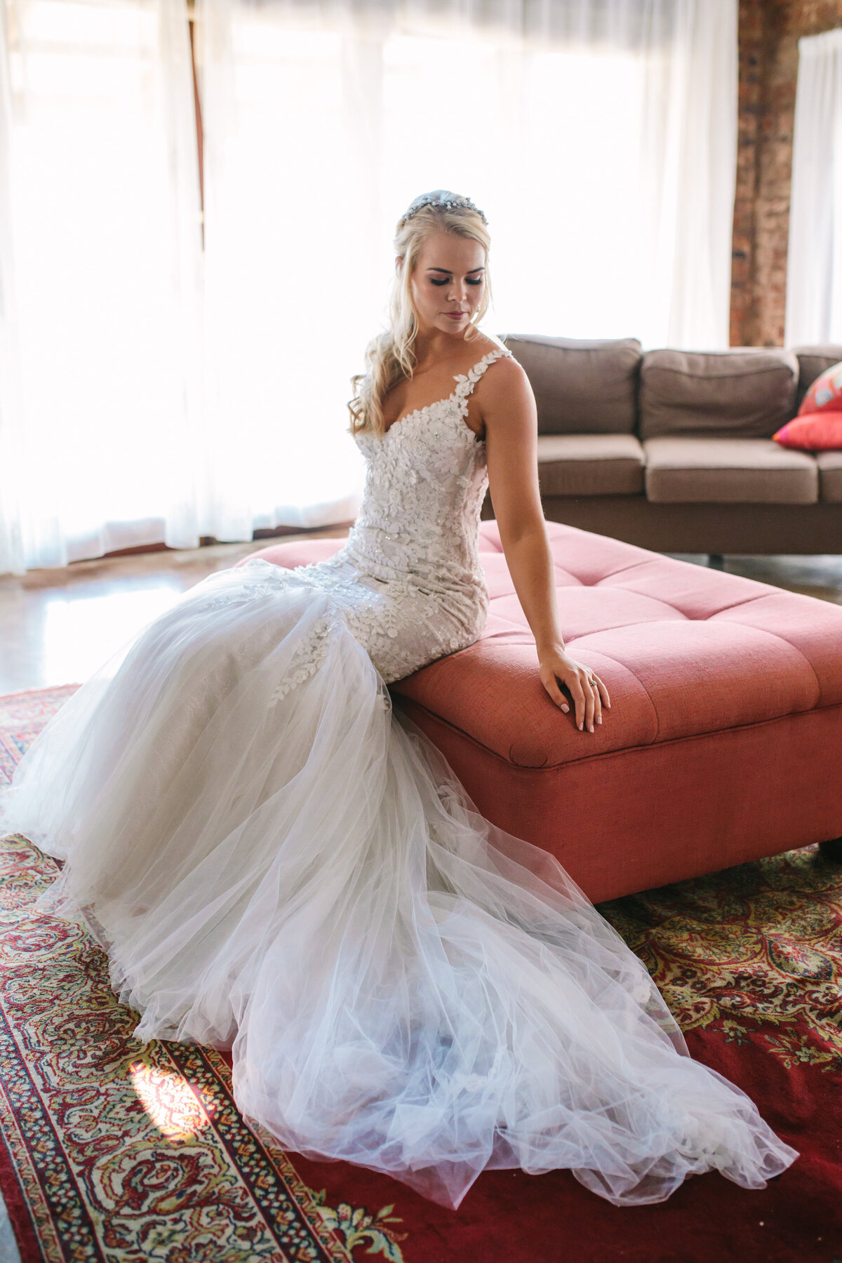 Bride sits on the edge of the chair with her dress draped over the carpet. 