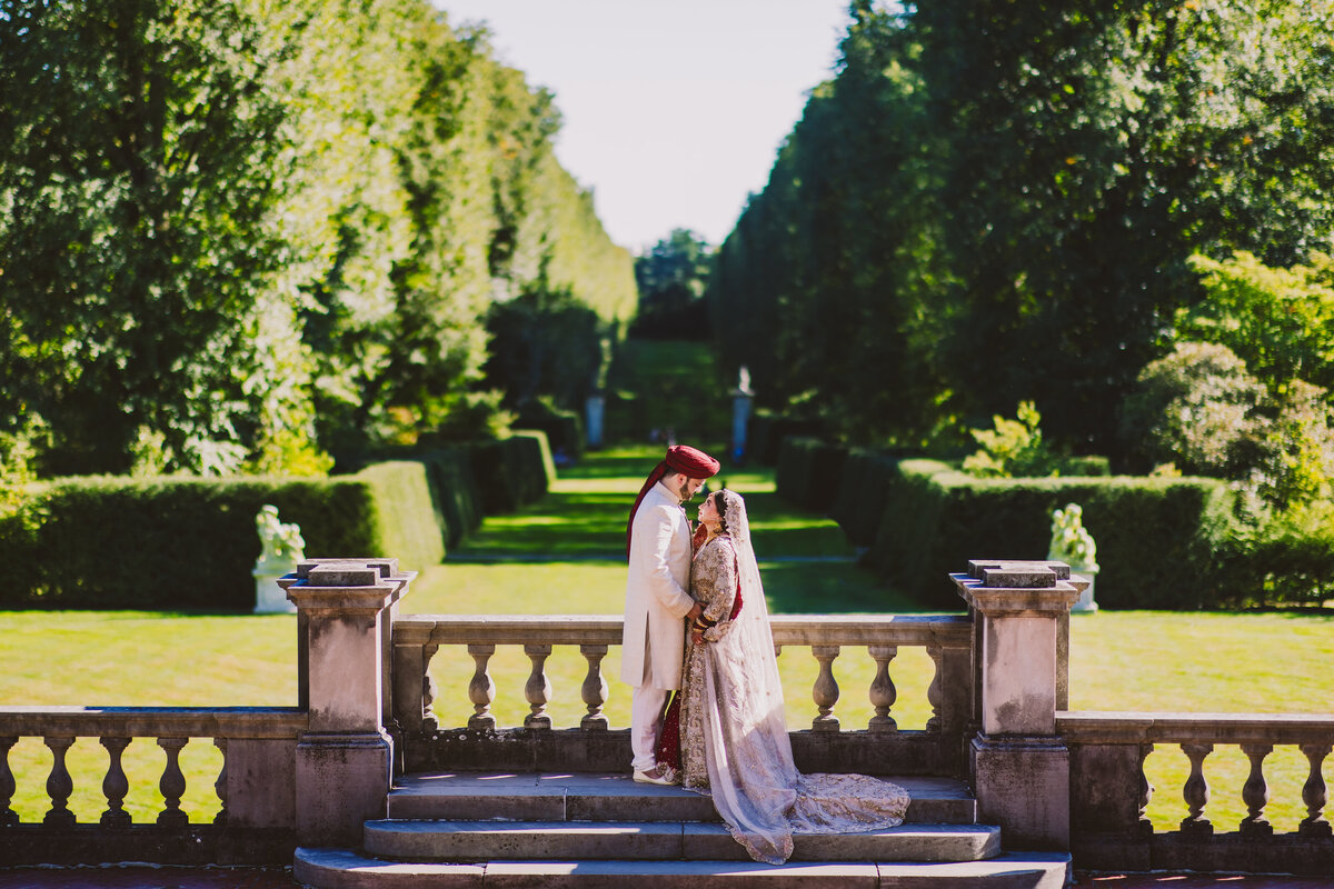 Pakistani muslim bride and groom hold hands and face each other overlooking the lawn at old westbury gardens in ny