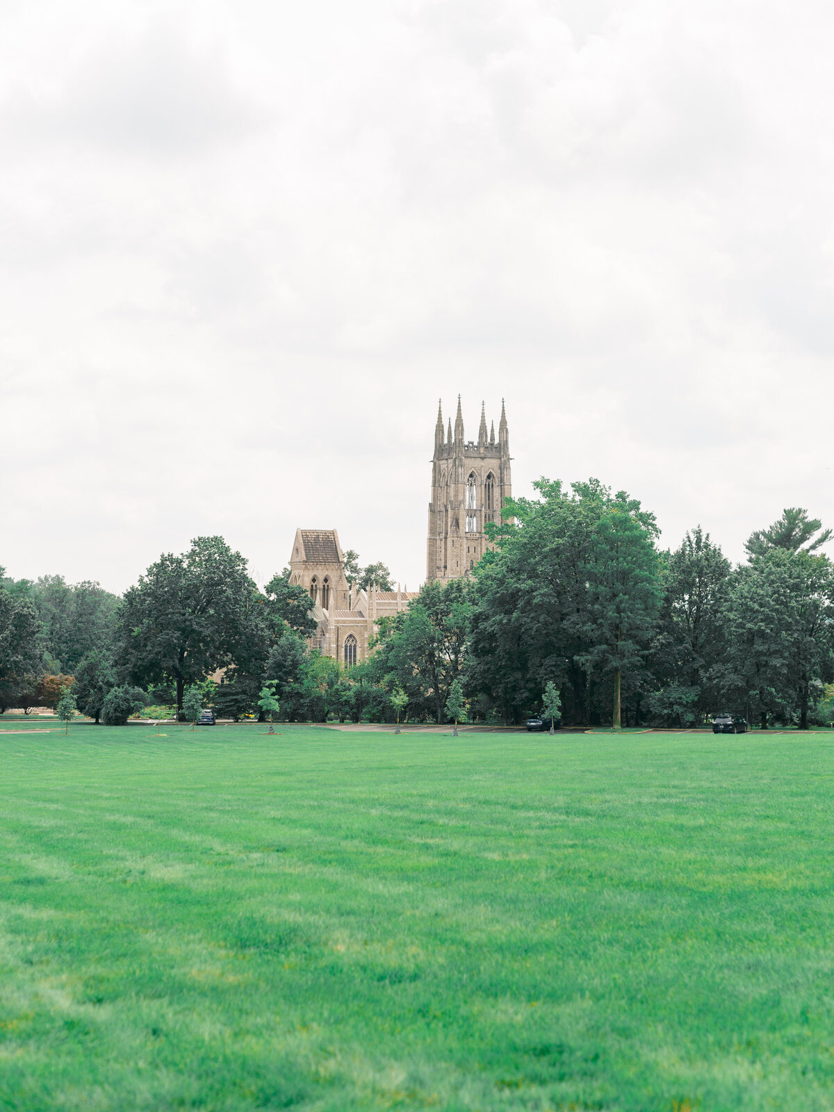 Bryn Athyn Cathedral rises beyond a wide expanse of manicured lawn, its soaring Gothic architecture framed by a canopy of trees. Captured by Elizabeth Kane Photography, a Luxury Philadelphia Wedding Photographer, this view evokes timeless grandeur and sacred romance.