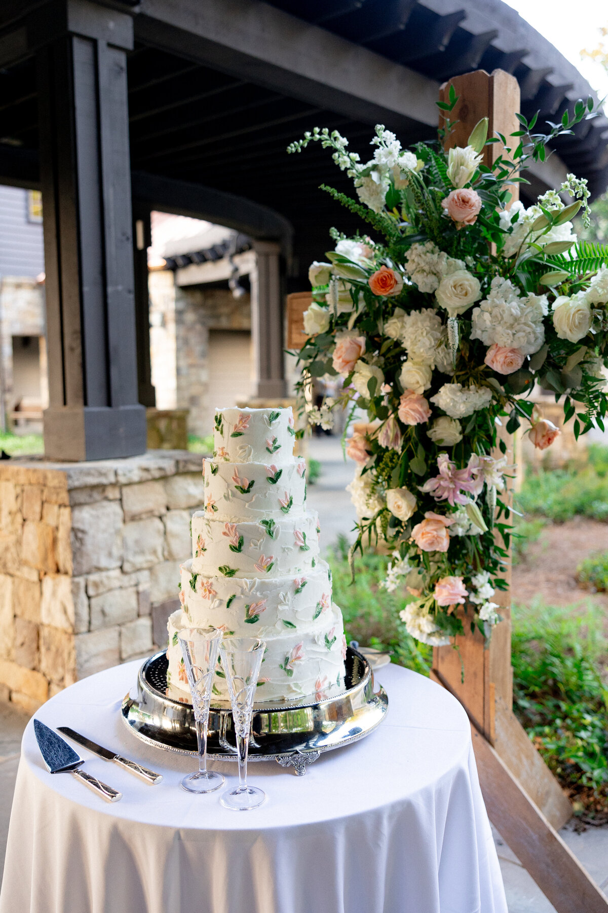 white cake sitting on a white circle table with a cross covered in flowers standing behind