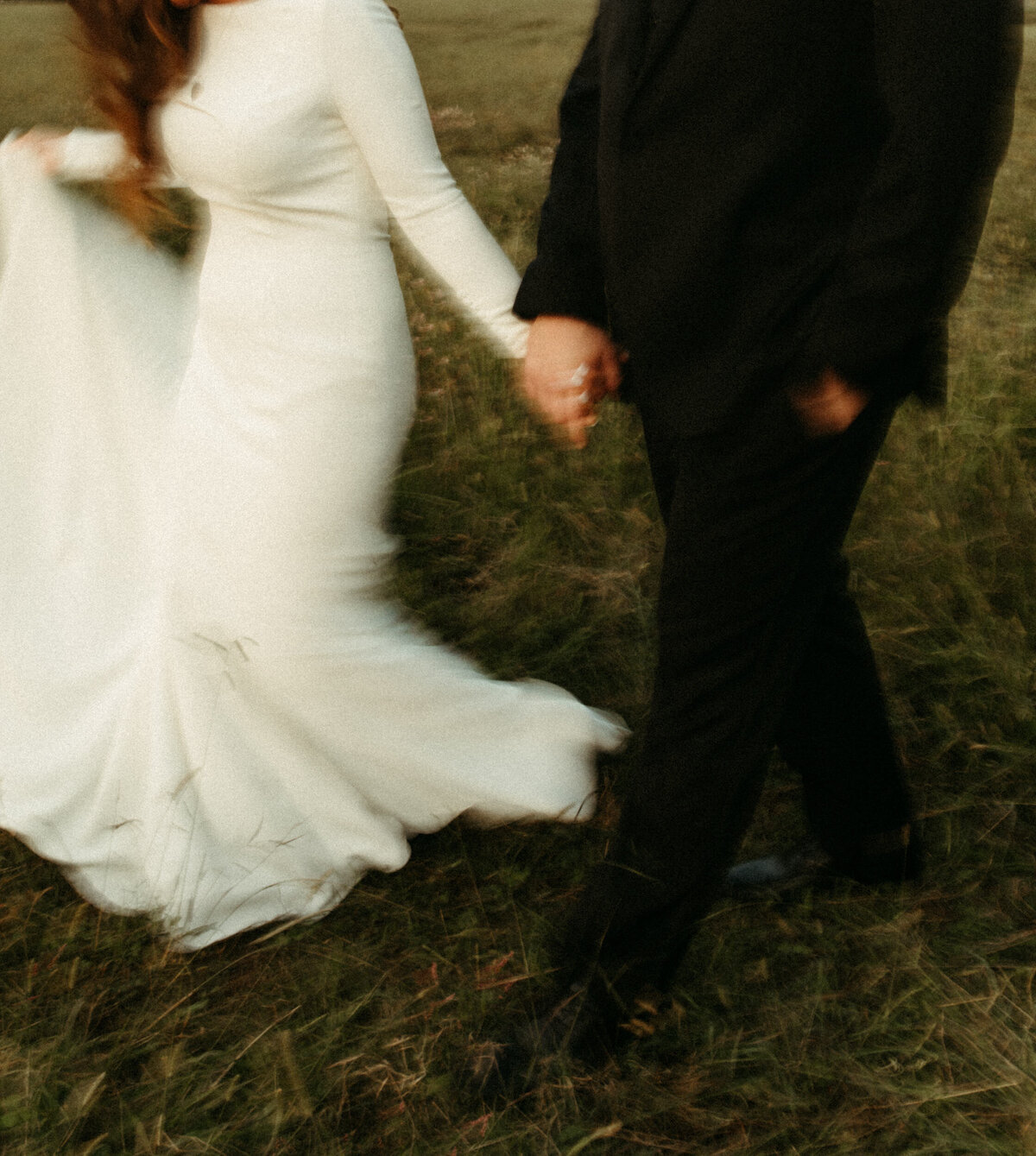 Bride in fitted dress with long sleeves holding hands with the groom with motion blur