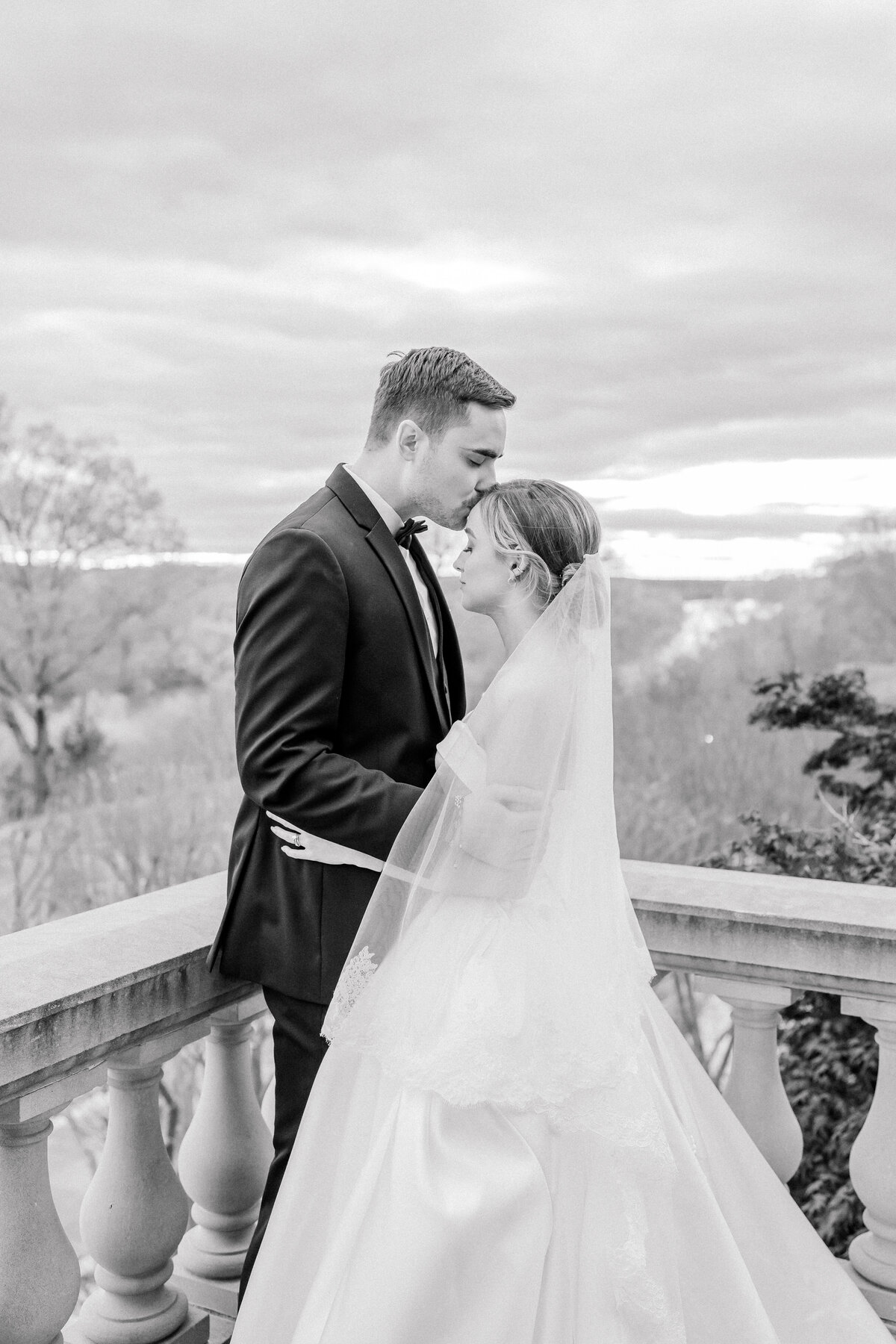 Black and white image of the groom kissing the bride on her forehead during sunset portraits