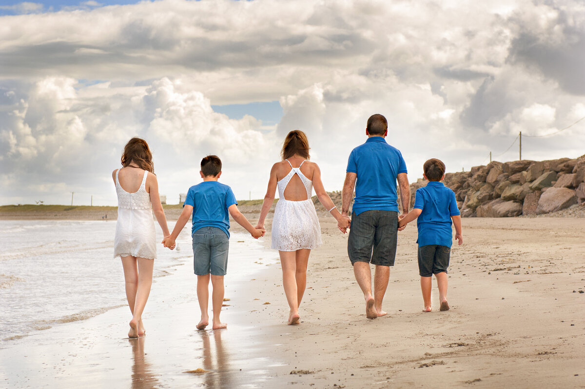 family of five on the beach wearing summer clothes, holding hands, walking away from the camera