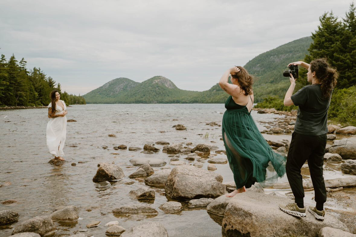 Two women look lovingly at each other as they look at each other from a distance across a lake in Acadia National Park during their elopement day