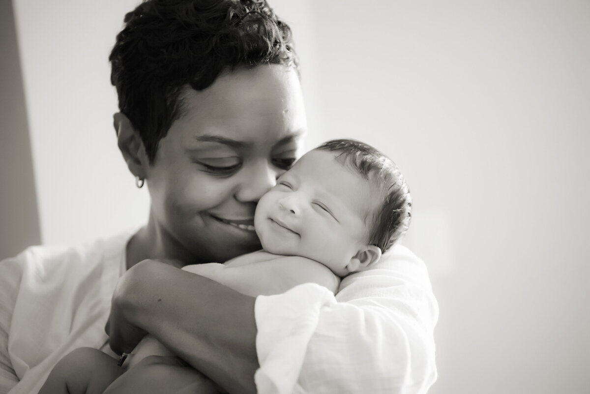 A parent holding their newborn with their nose on their cheek 