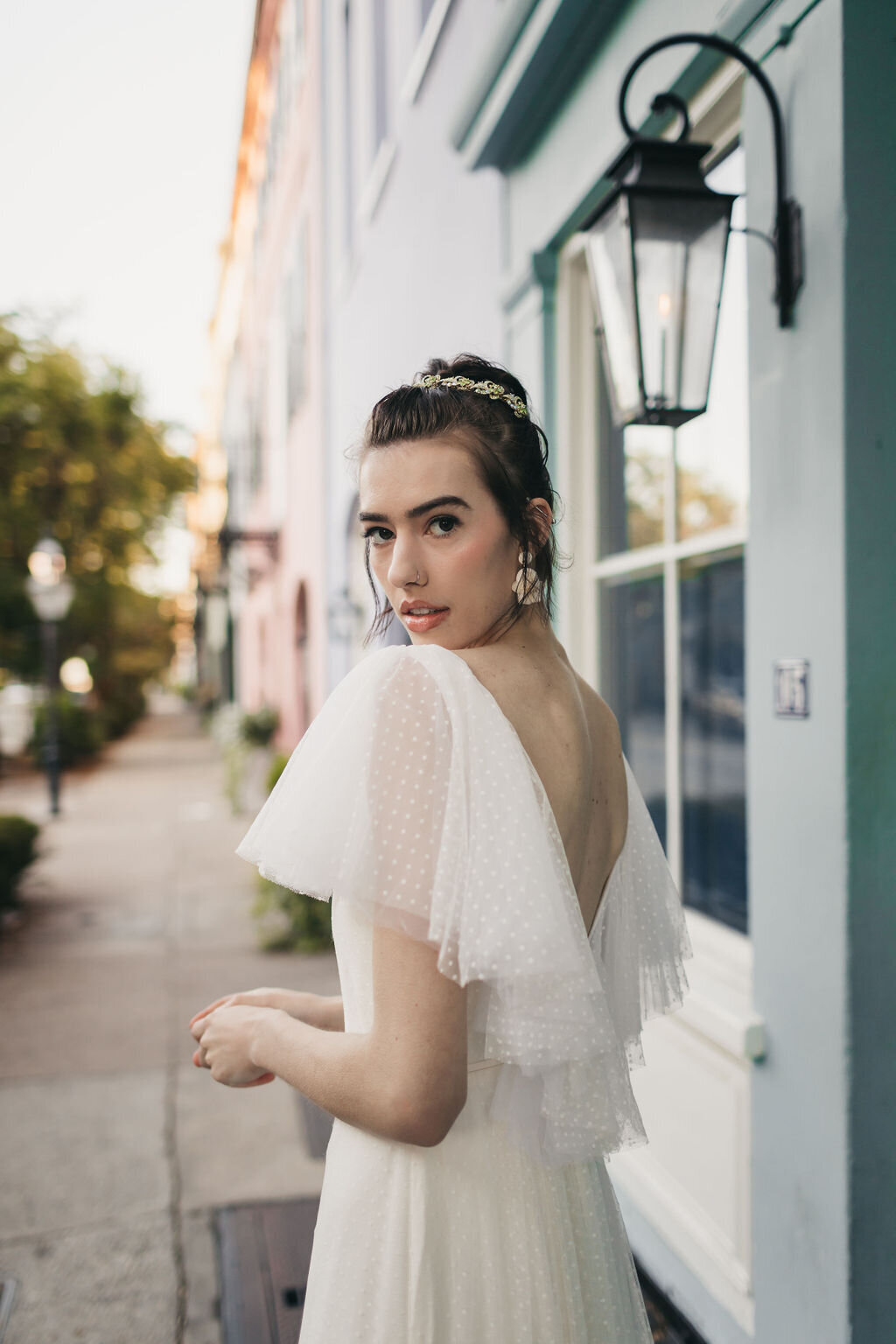 A close-up of the flutter sleeves and v-back on the Mai wedding dress style as it's modeled in front of downtown Charleston's iconic Rainbow Row.