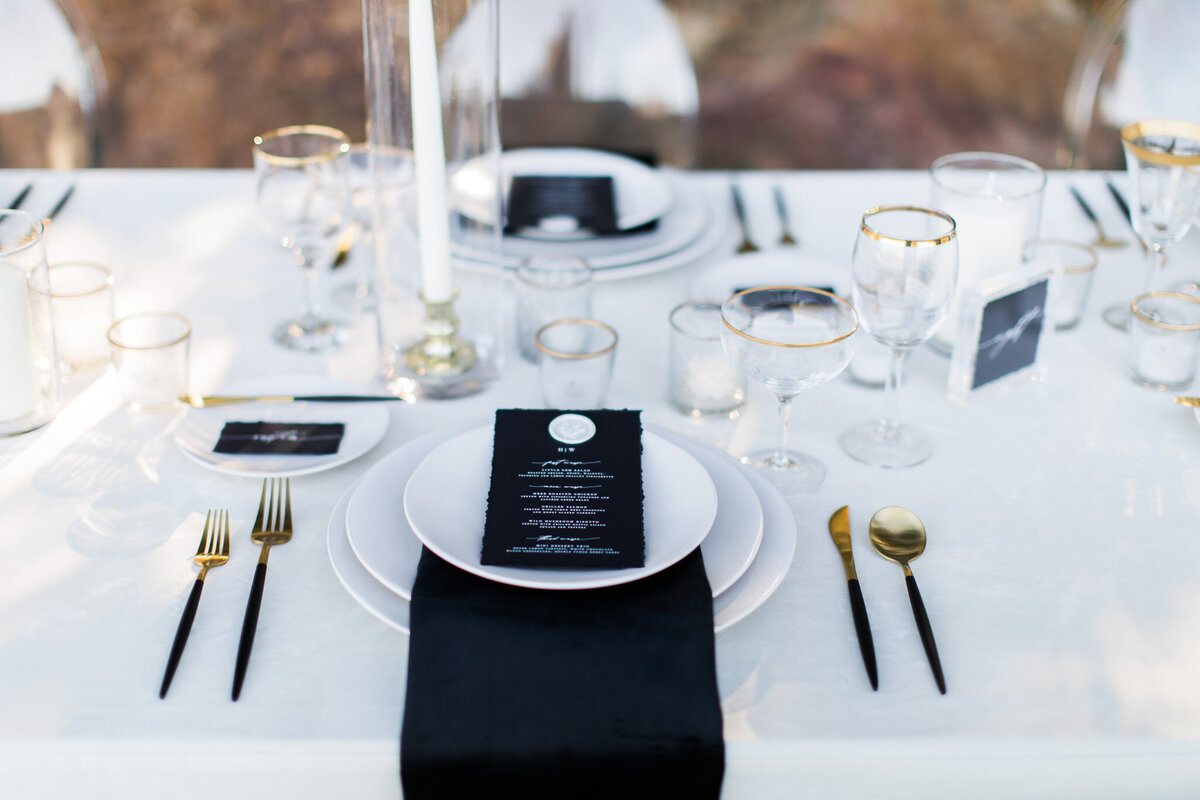 Luxury wedding table setting featuring black accents, white linens, and ghost chairs.