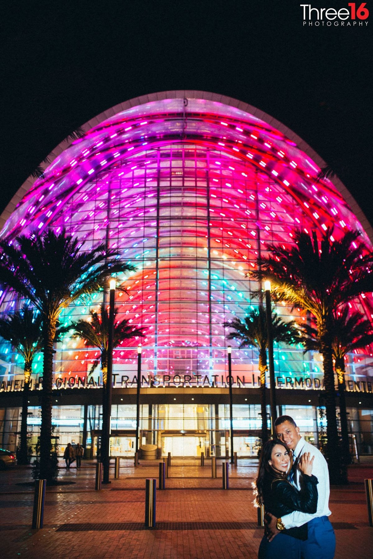 Couple pose in front of the beautiful lights of the ARTIC Train Station in Anaheim