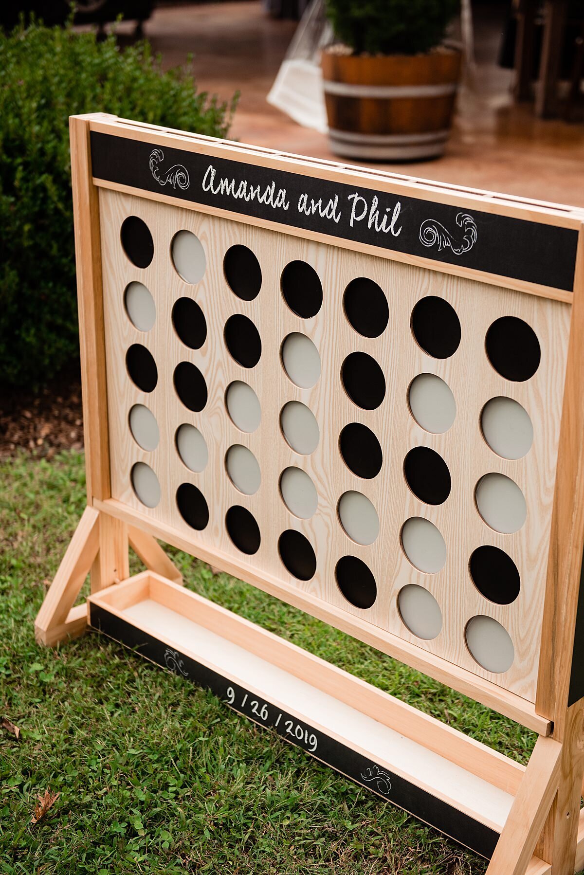 Giant connect four wedding lawn game in a light wood frame with white and black checkers personalized.