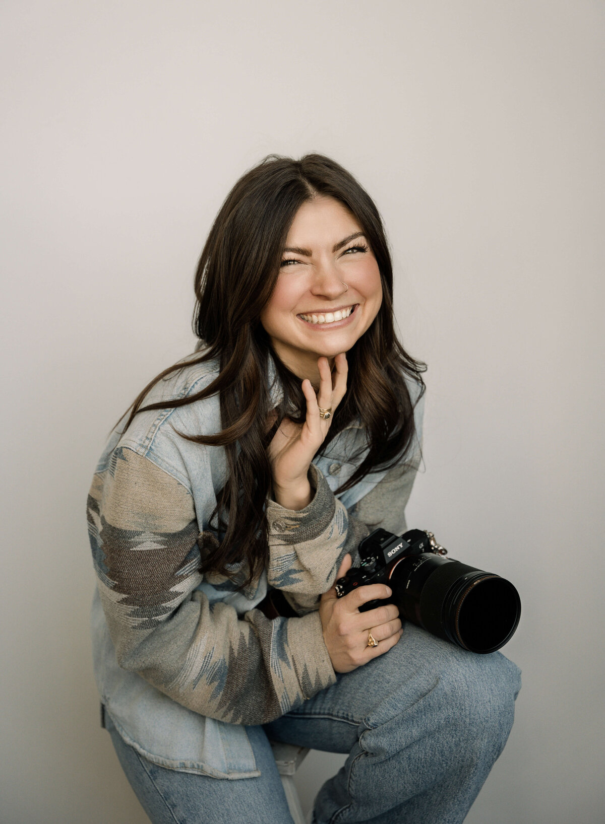 A young woman laughs, while looking at the camera while holding a camera