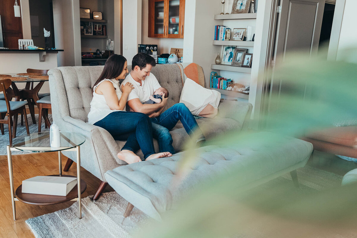 new parents sit on their living room couch admiring their newborn son during their lifestyle newborn session with Christine Dammann photography