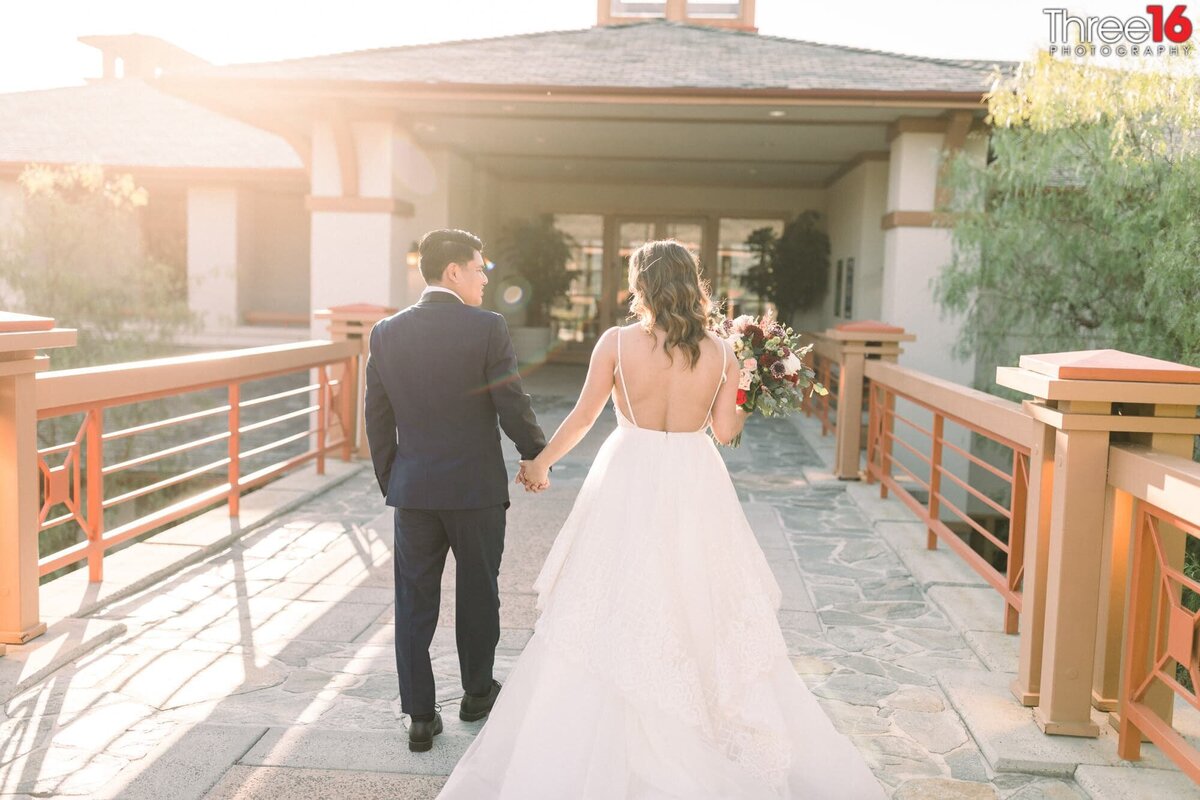 Bride and Groom walk across a bridge holding hands