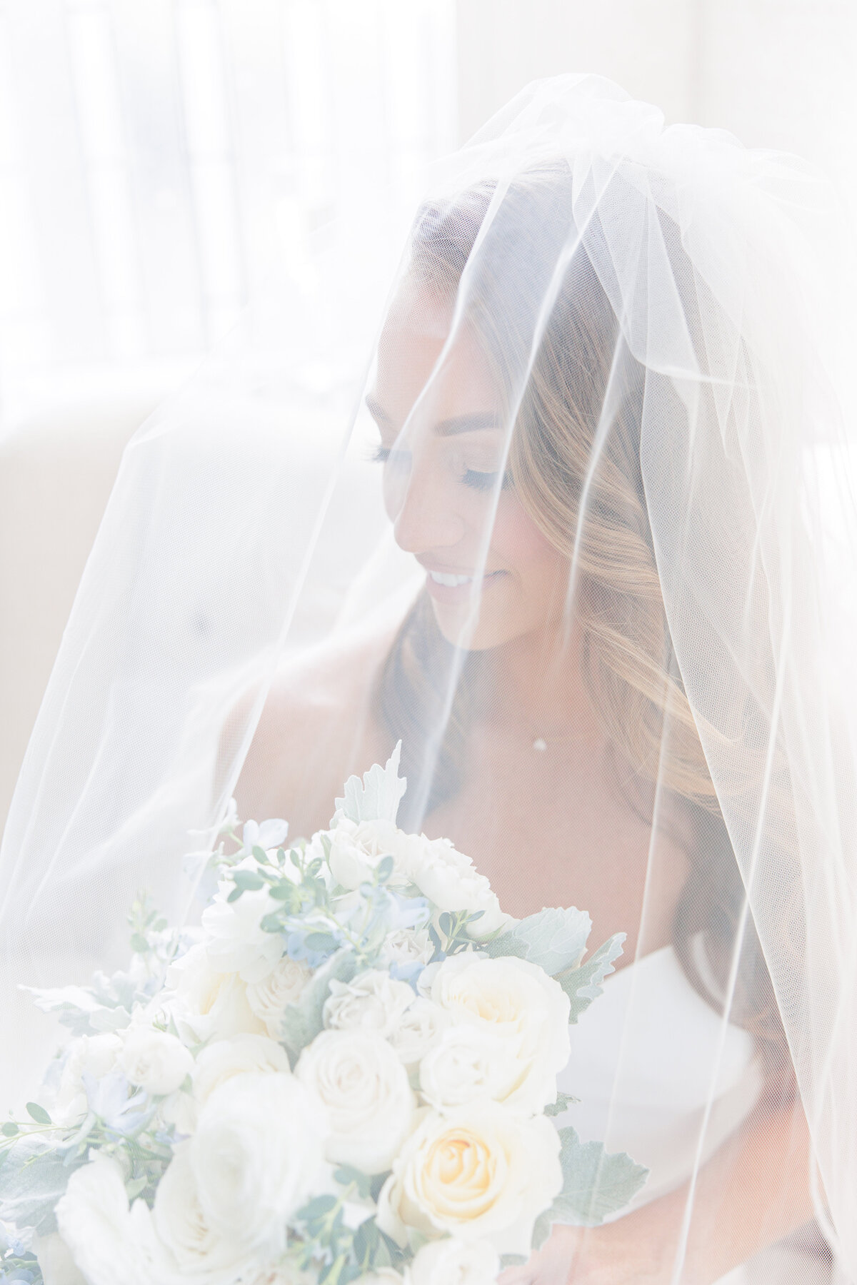 Bride looking at her bouquet underneath her veil representing Boston bridal portraits