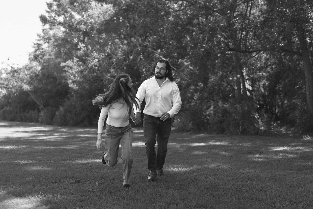 black and white photo of a couple running outside while holding hands.