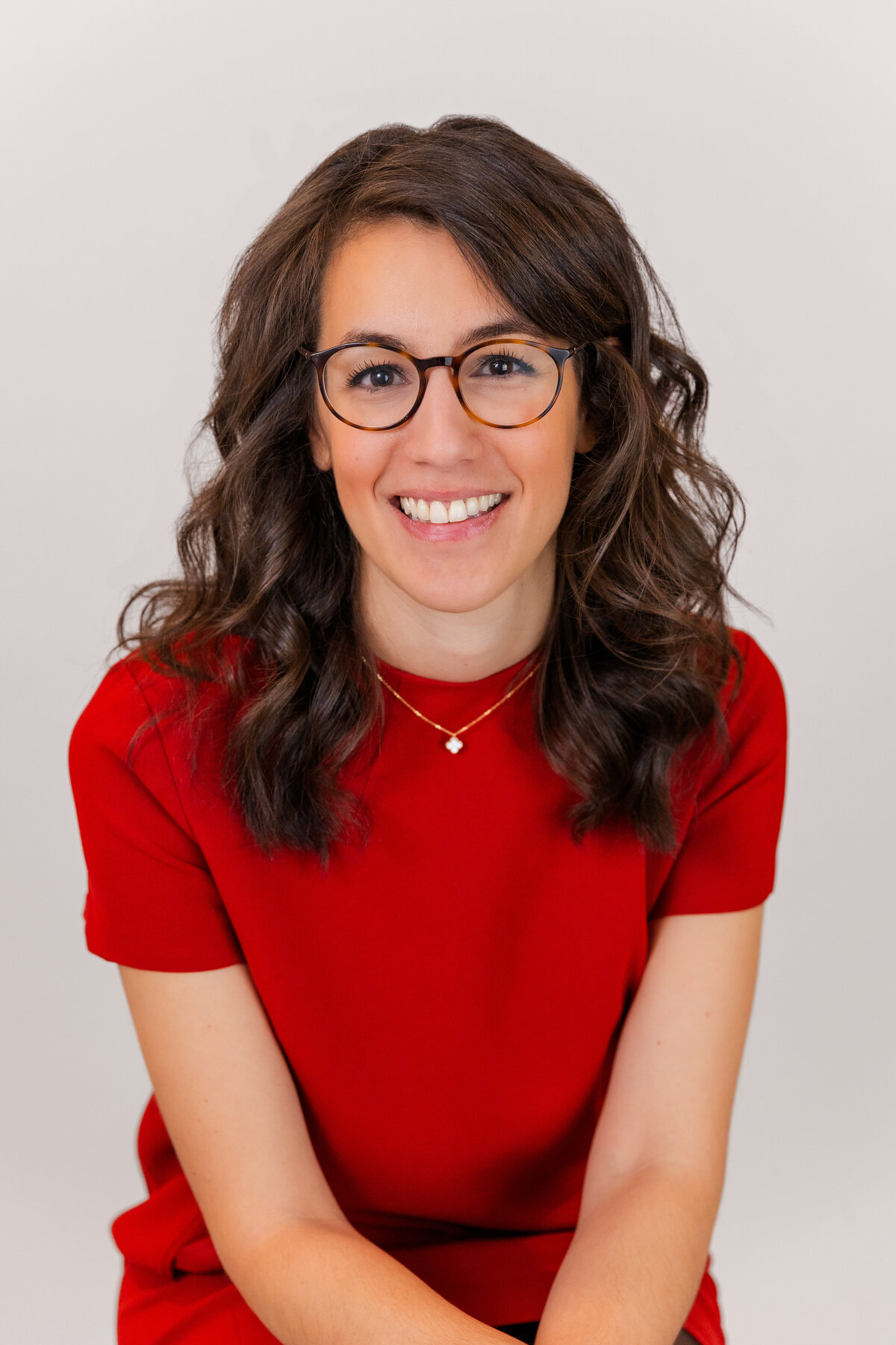 woman wearing a red dress sitting hands together in front of a light gray backdrop during portraits session