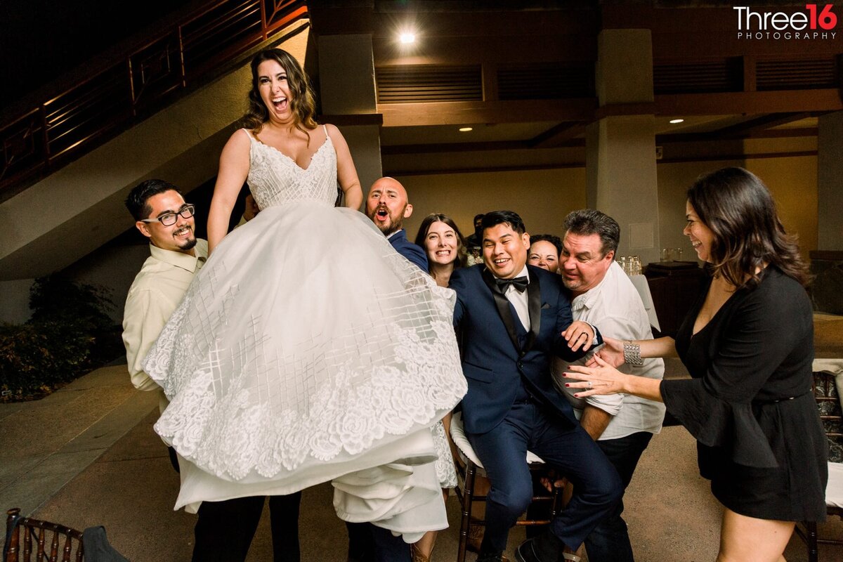 Male wedding guests lift the Bride up in the air