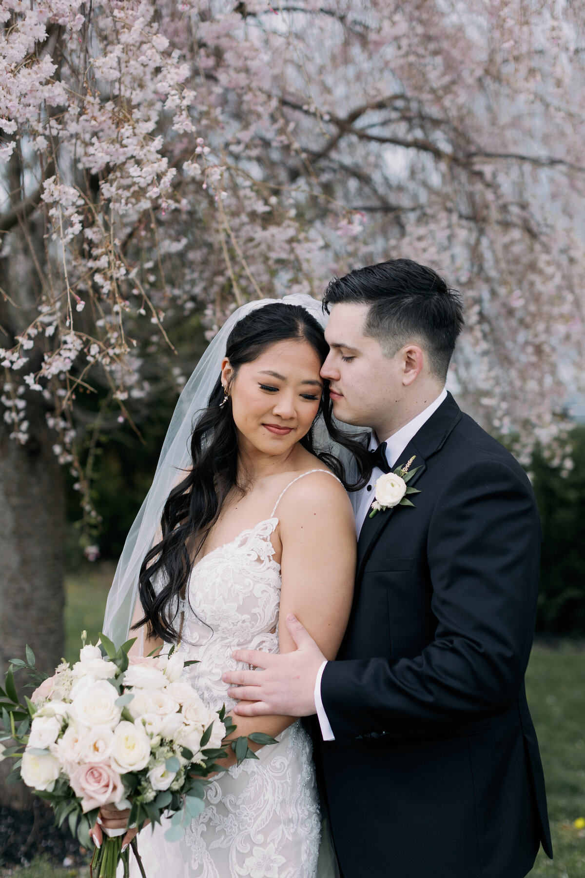 Bride and groom stand under a fully bloom cherry blossom tree for their bridal portraits